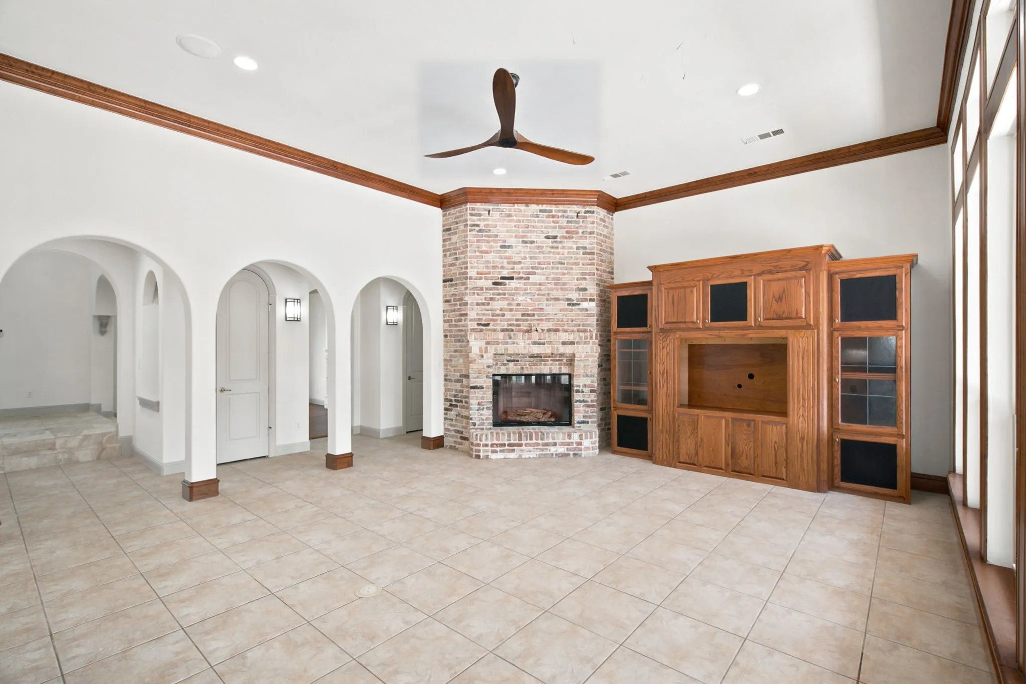 Vaulted ceiling, brick fireplace, extensive built-in media cabinetry, tile flooring, and arched doorways