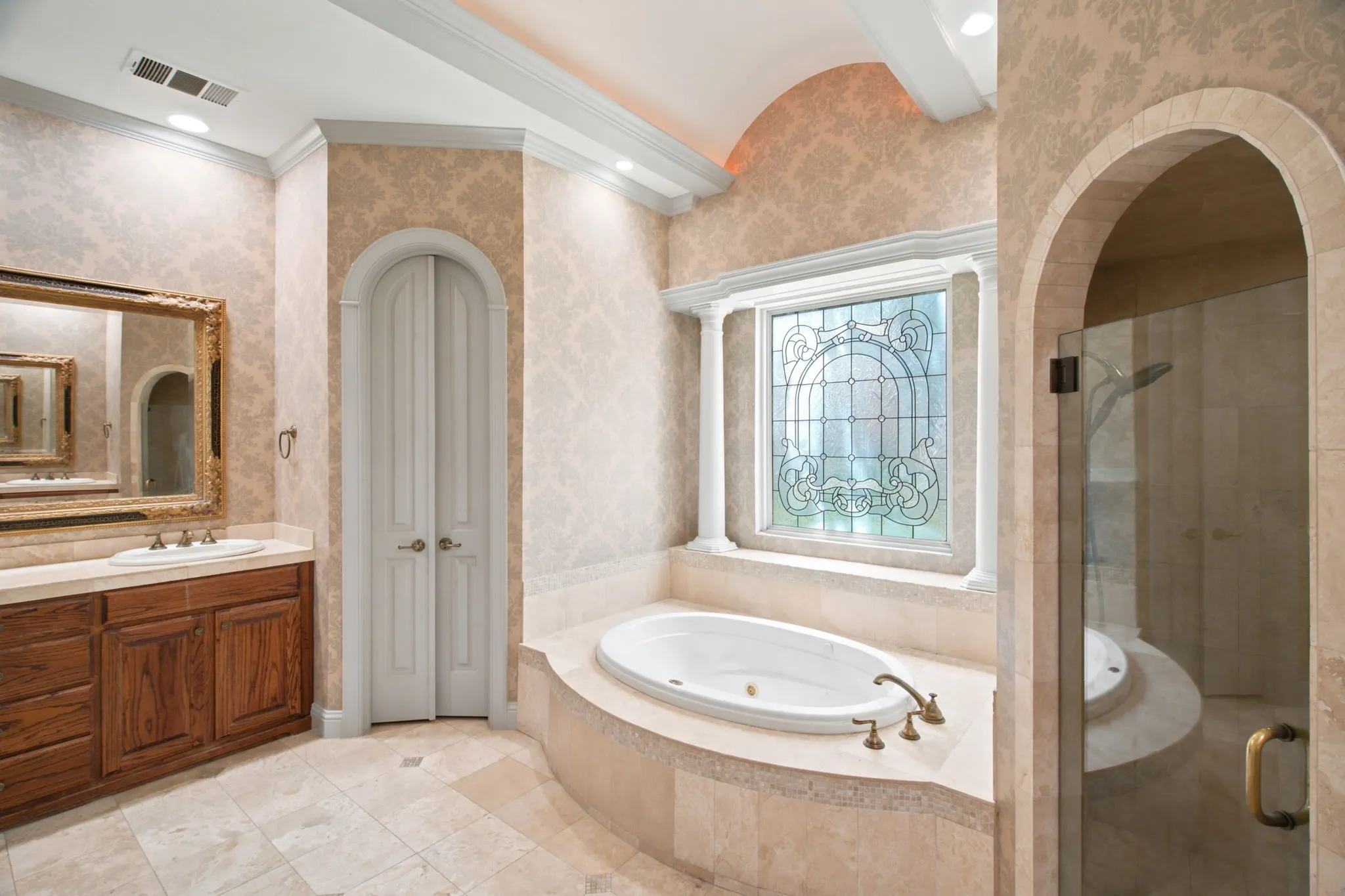 Built-in soaking tub, leaded glass window, arched shower entrance with glass enclosure, wood vanity with integrated sink, and tile flooring
