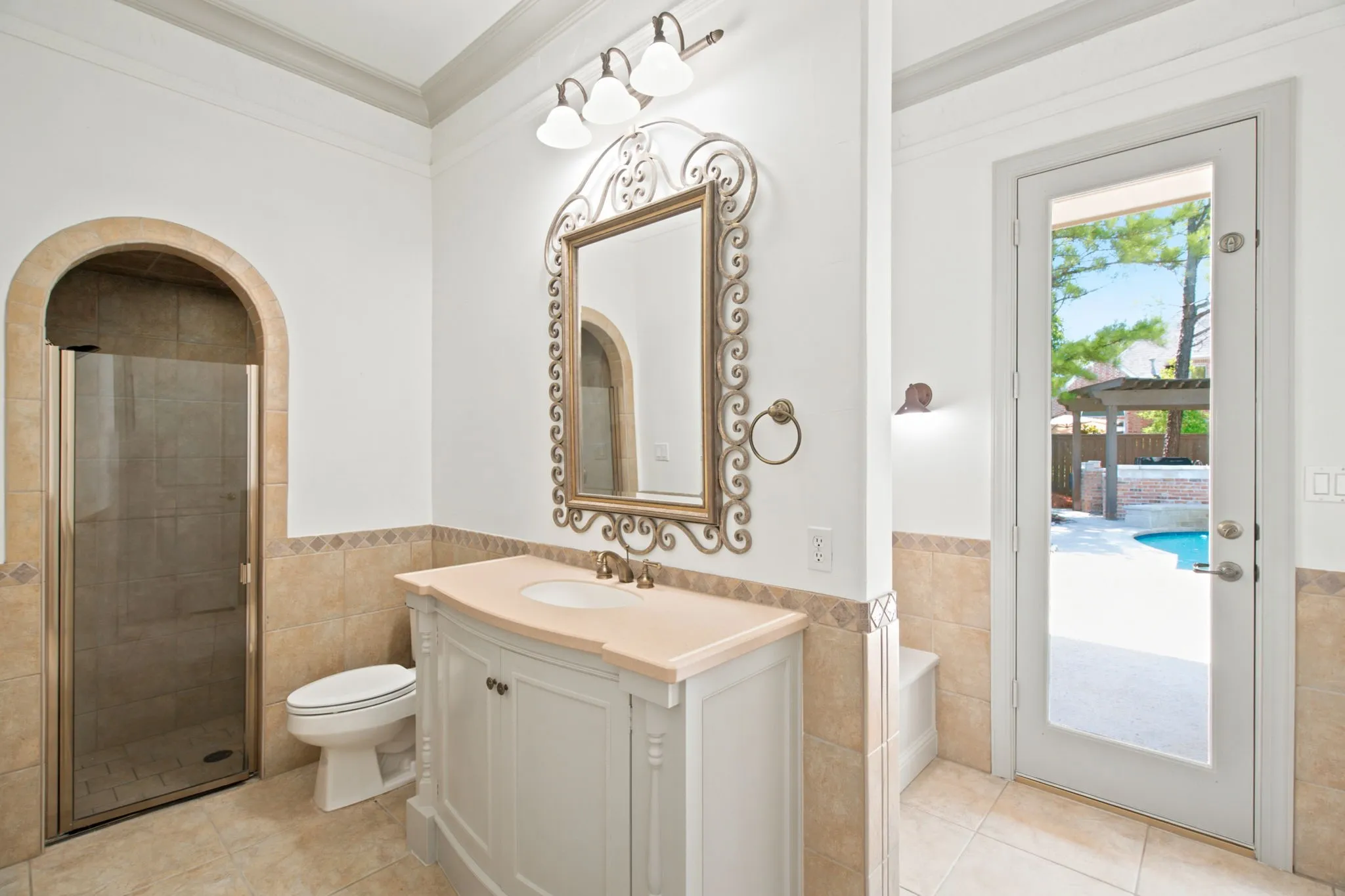 Single vanity with a light-toned countertop, arched shower enclosure with glass door, and a full-light exterior door