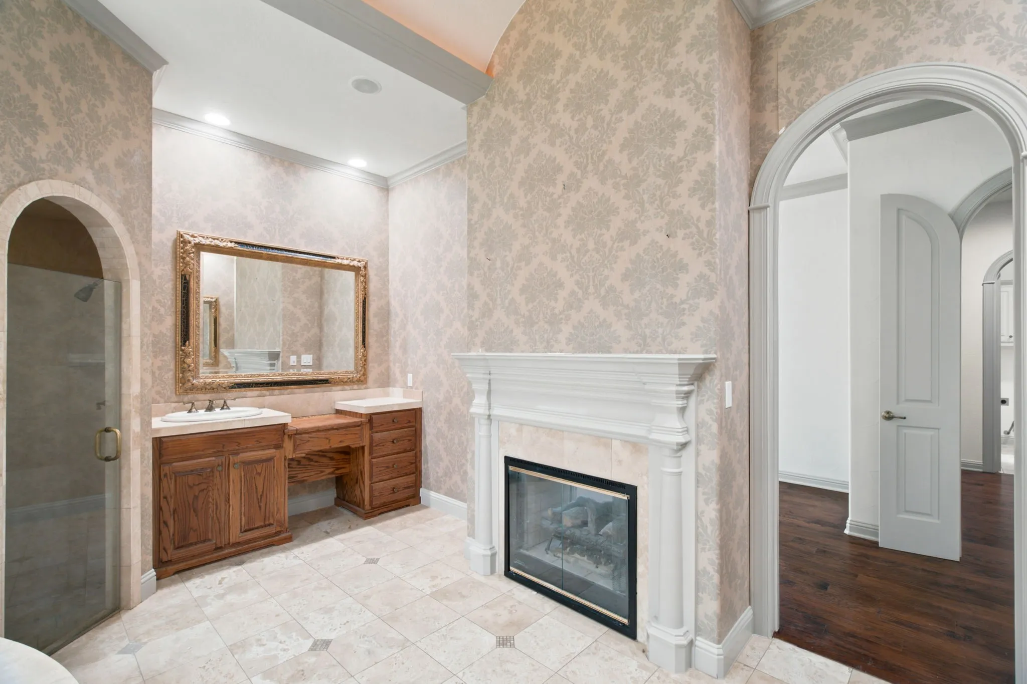Tiled flooring, wood vanity with integrated sinks, framed mirror, built-in fireplace, and arched doorways