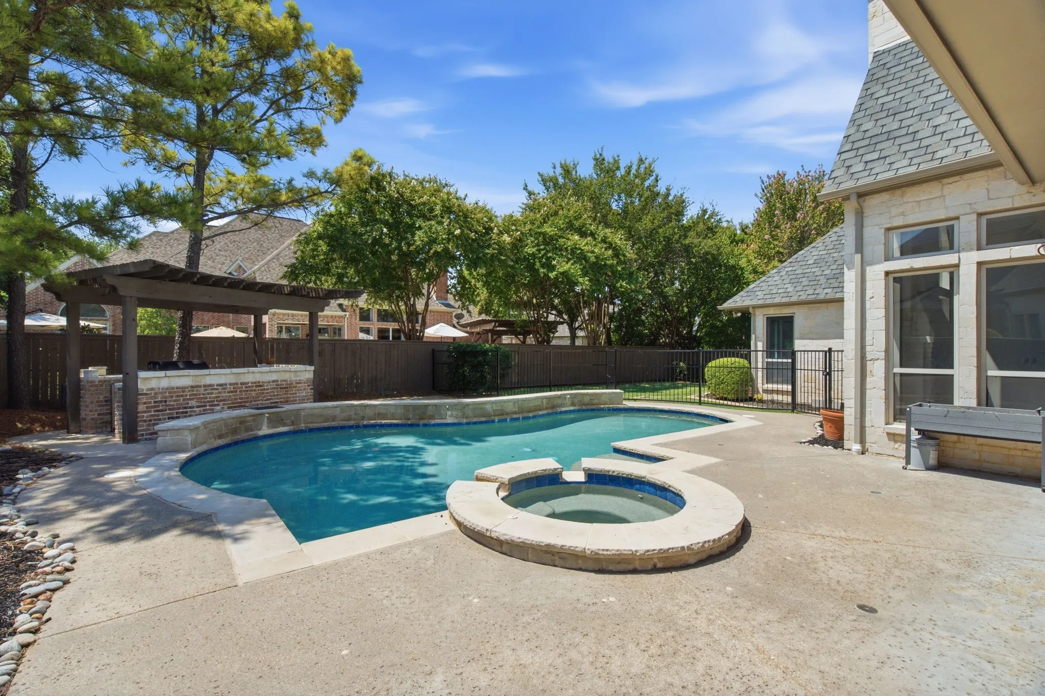 Backyard featuring a freeform swimming pool, integrated spa, and an outdoor kitchen with a pergola