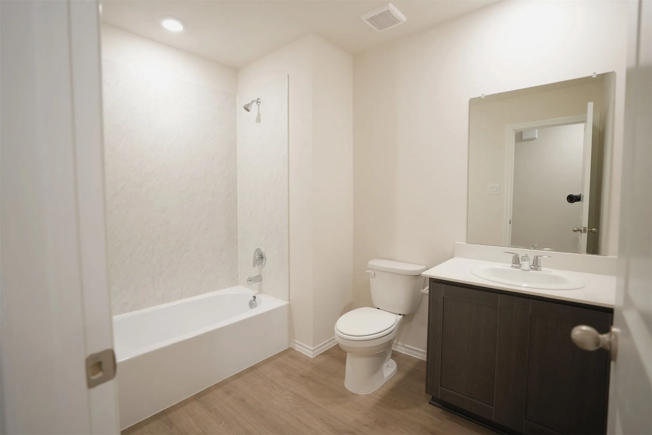 Bathroom featuring a full tub with shower, wood-finish flooring, a vanity with integrated sink and storage, and a wall-mounted mirror