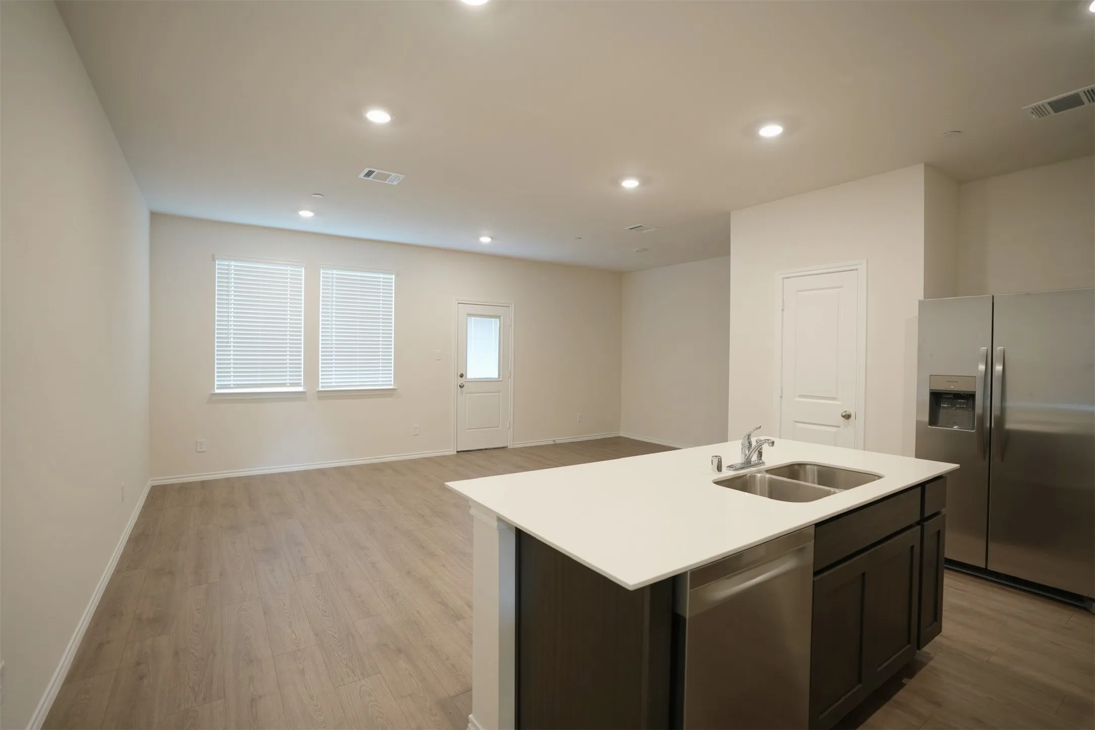 Open-concept living space featuring wood-finish flooring, recessed lighting, and a kitchen island with an integrated double basin sink and stainless steel dishwasher