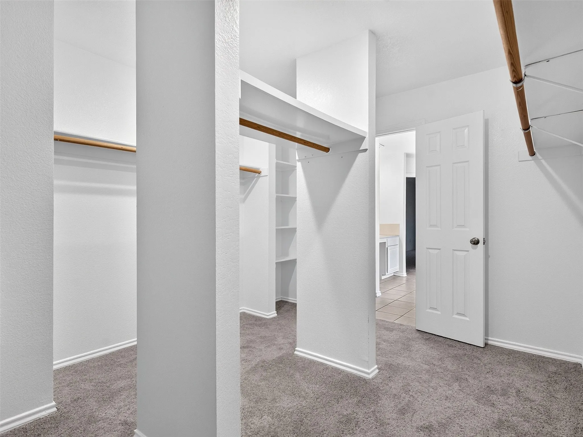 Walk-in closet featuring built-in shelving, multiple hanging rods, white walls, white baseboards, and gray carpet flooring