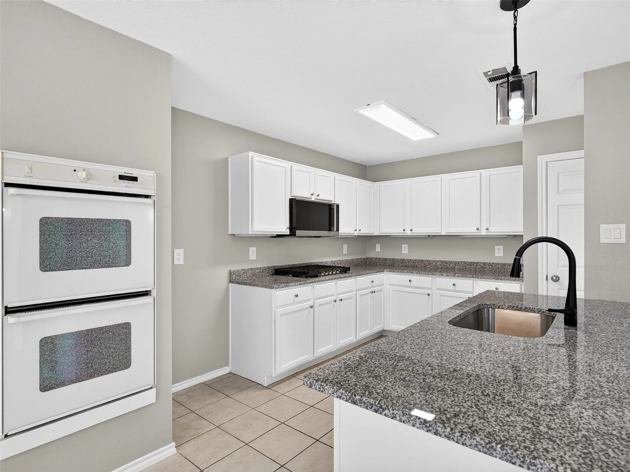 Kitchen featuring white shaker-style cabinetry, dark speckled countertops, and tile flooring