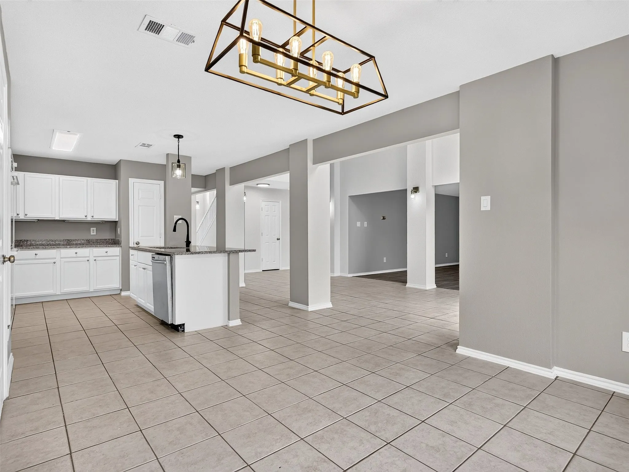 Kitchen and living area featuring a modern chandelier, tile flooring, white cabinetry, granite-style countertops, and a kitchen island with a built-in sink and dishwasher