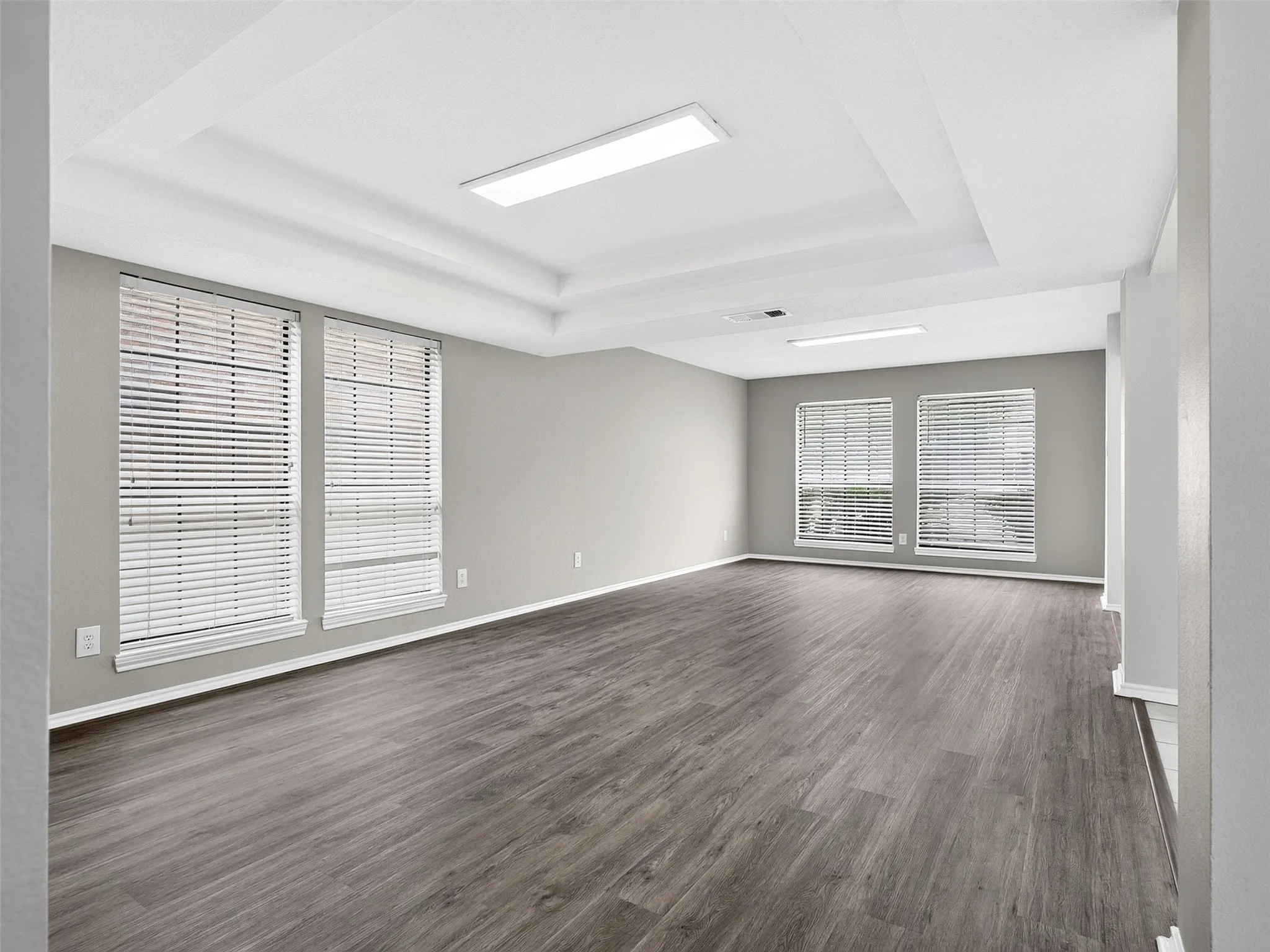 Spacious room with wood-finish flooring, light grey walls, and a tray ceiling