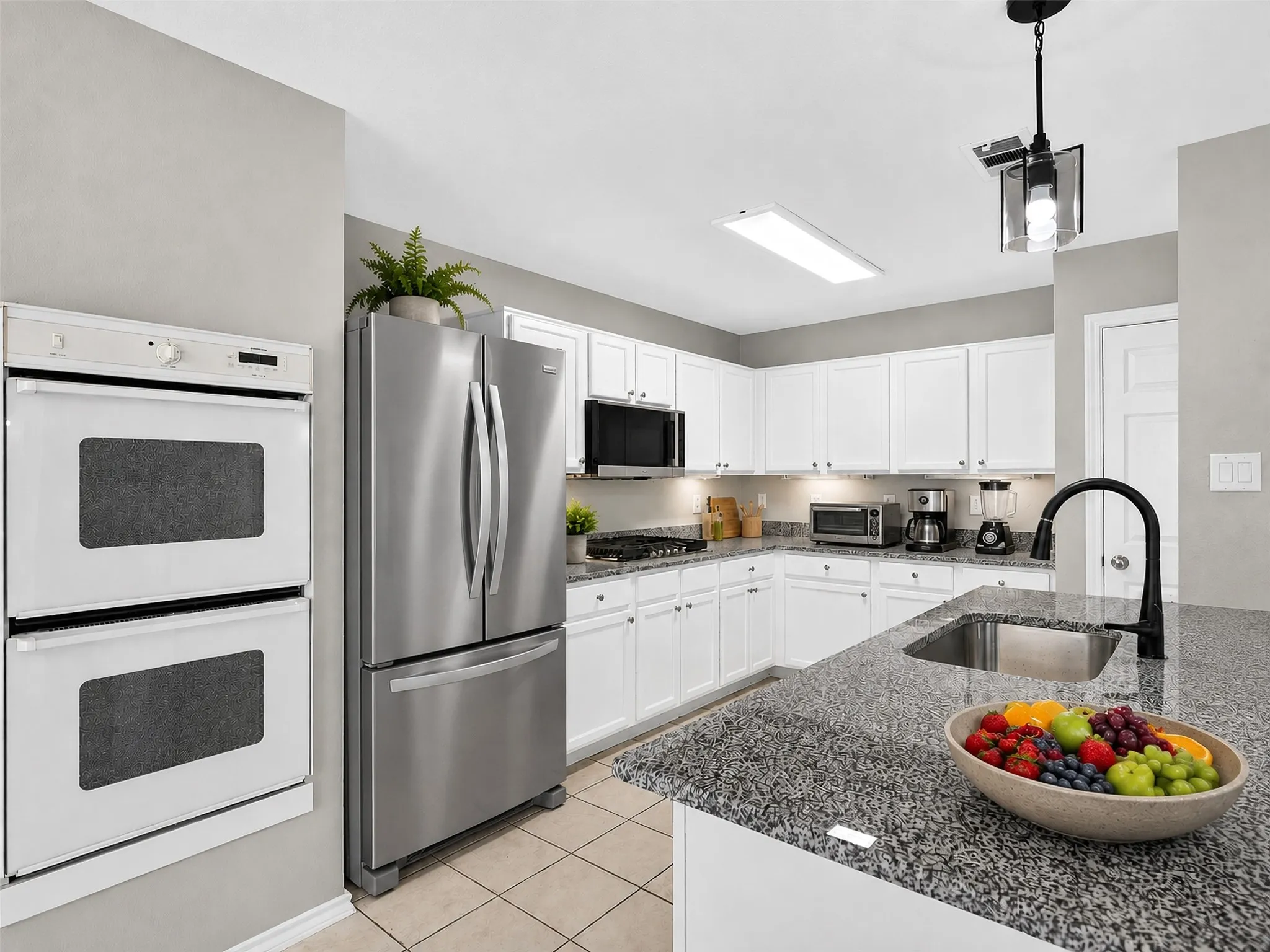 Modern kitchen featuring granite countertops, white cabinetry, a stainless steel refrigerator, and dual built-in ovens