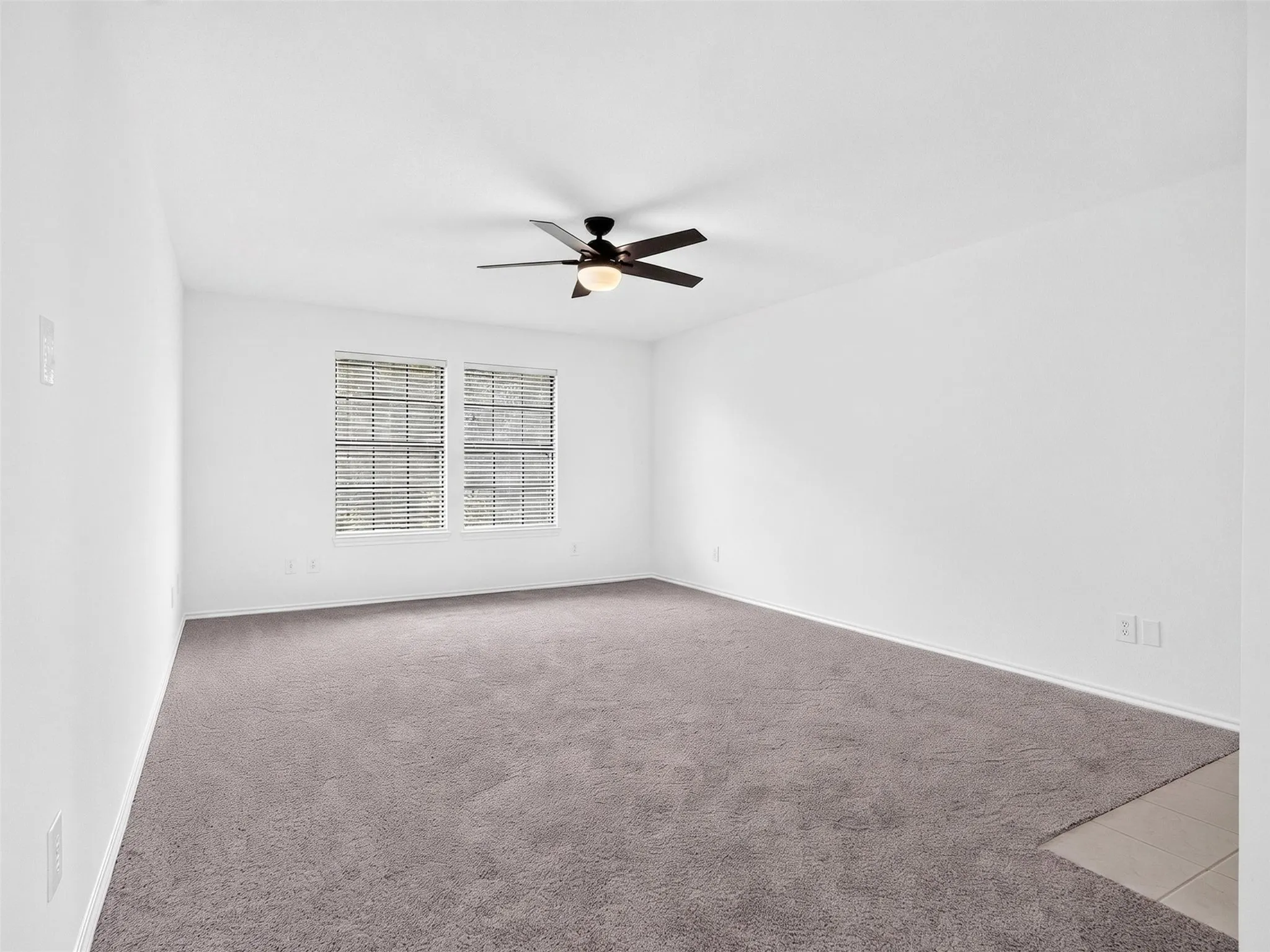 Spacious room featuring white walls, gray carpet, a ceiling fan with light, and two windows with blinds