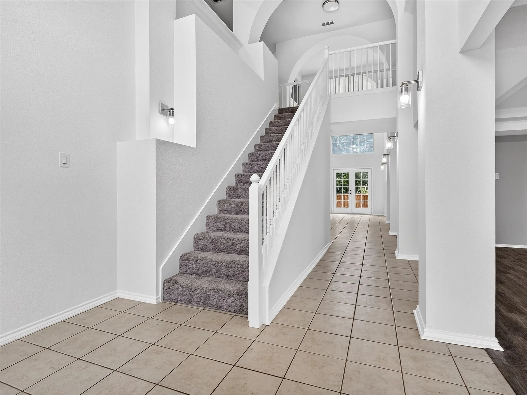 Grand foyer featuring a carpeted staircase with white railings, tile flooring, and arched architectural details