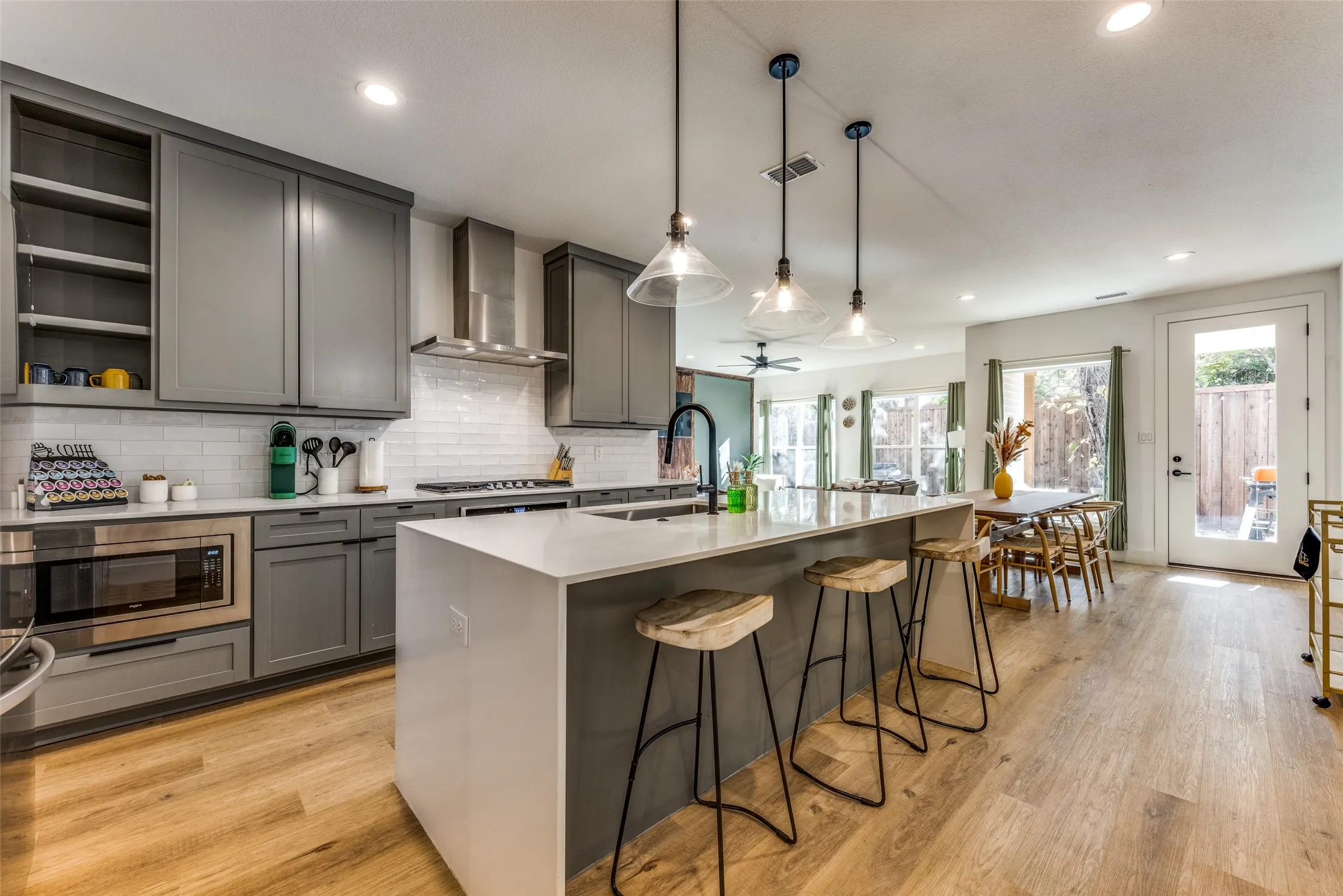 Open-concept kitchen featuring an oversized island with seating, pendant lighting, stainless steel appliances, and wood-finish flooring