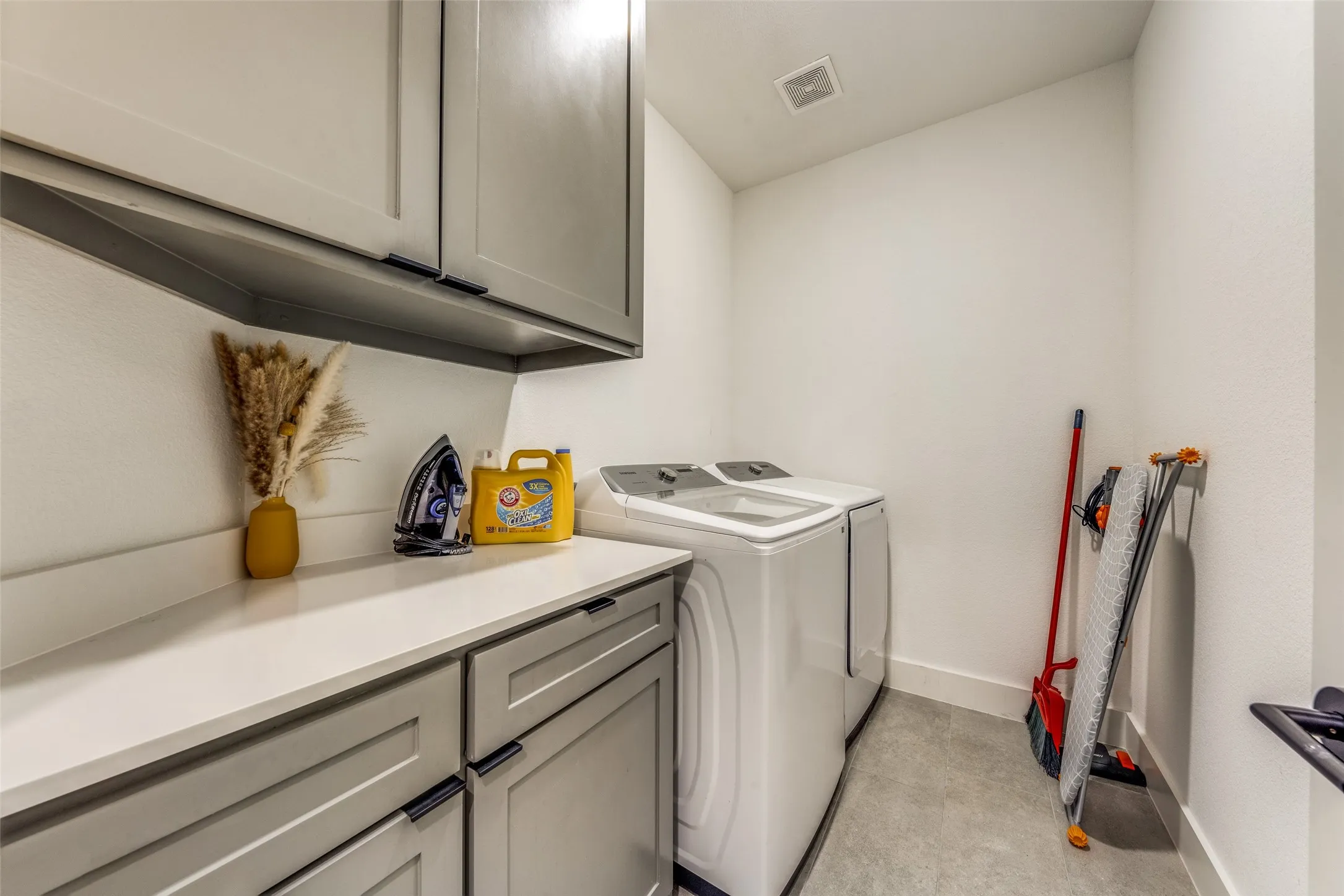 Dedicated laundry area featuring a light countertop, gray cabinetry with black hardware, and tile flooring