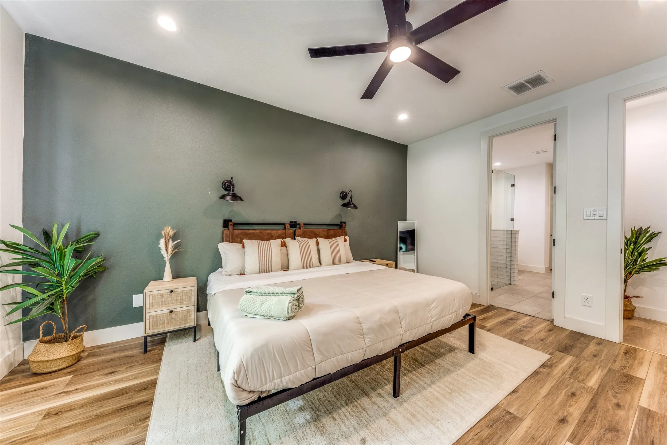 Bedroom featuring a dark accent wall, wood-finish flooring, a contemporary ceiling fan with integrated lighting, recessed lighting, and a doorway to a bathroom with tiled walls