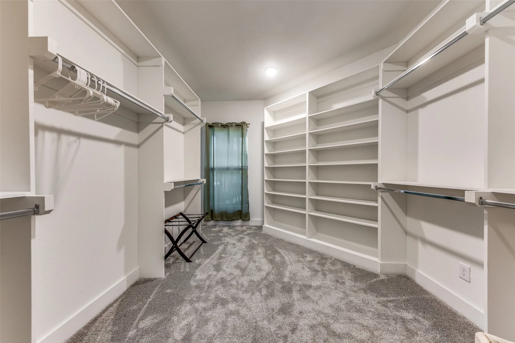 Spacious custom closet featuring extensive built-in shelving, multiple hanging rods, and plush gray carpeting