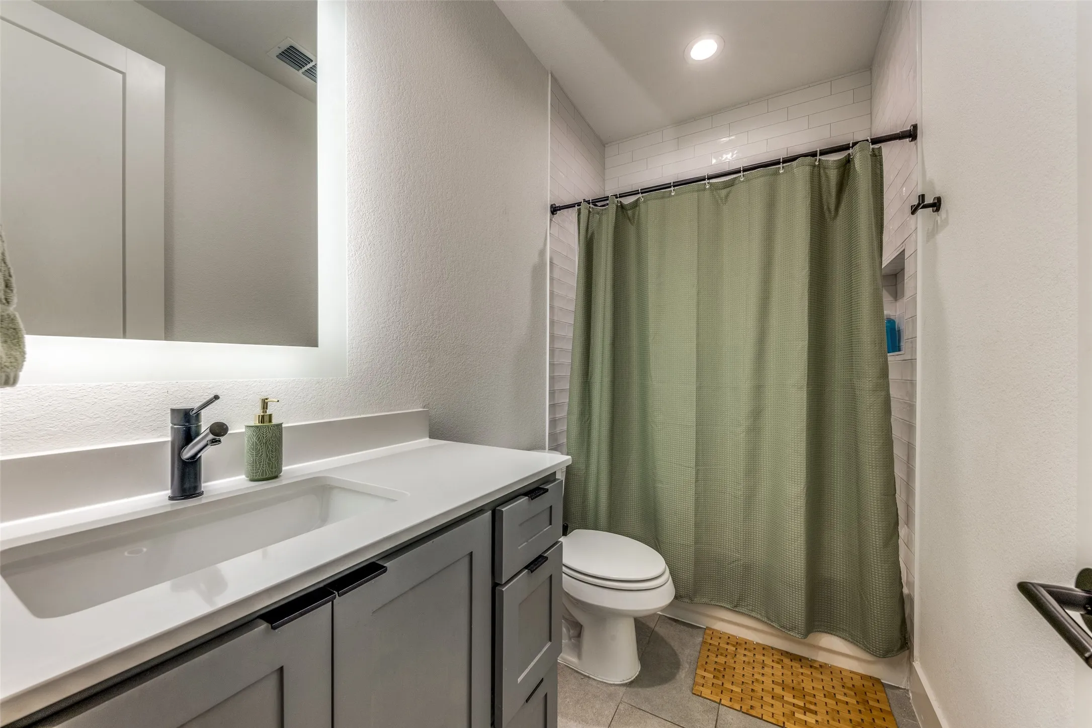 Bathroom featuring a white subway tile shower surround with a built-in niche, a toilet, a vanity with a white countertop and an integrated sink, and gray cabinetry with black hardware