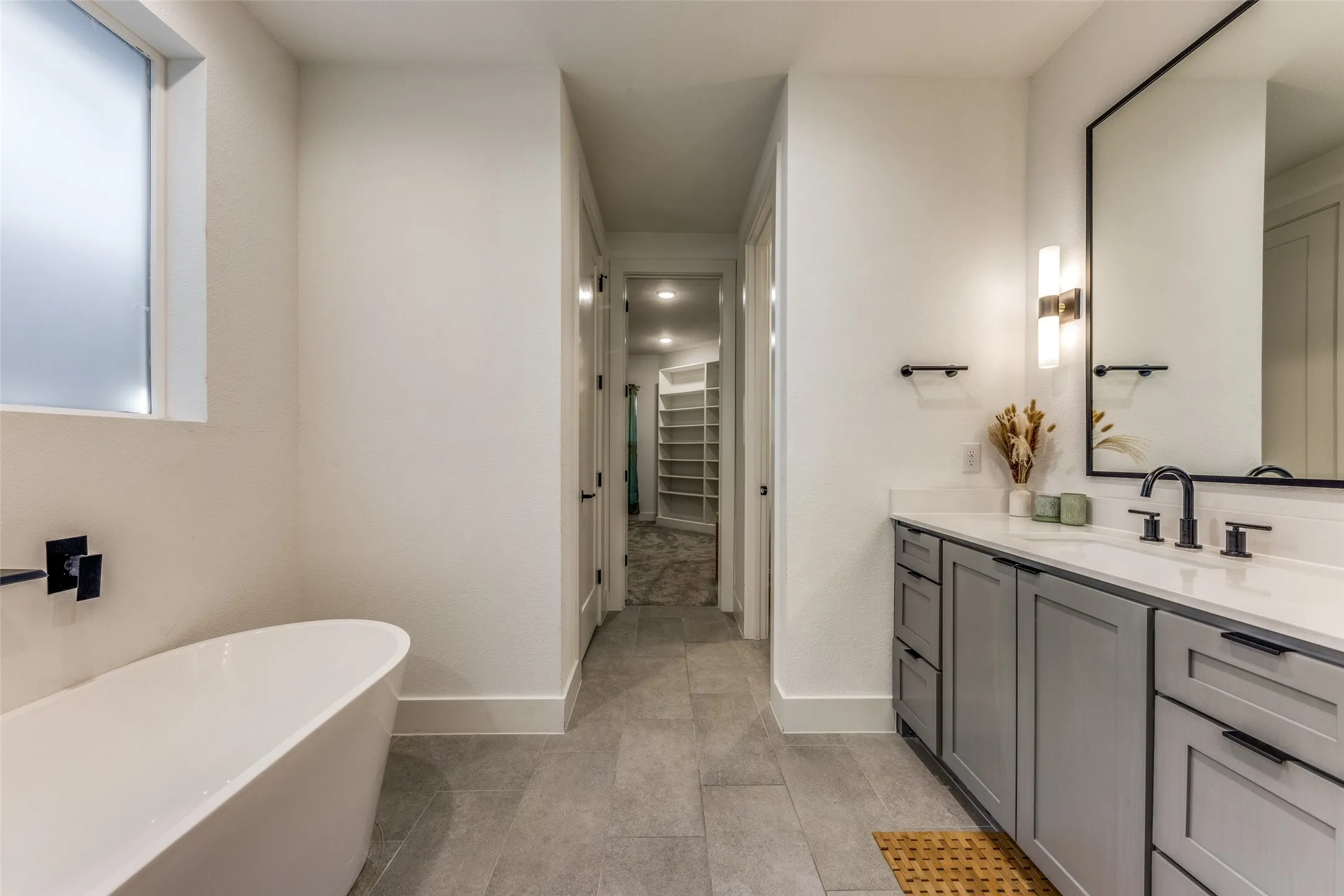Contemporary bathroom featuring a freestanding tub, a vanity with gray cabinetry and matte black hardware, and a large framed mirror