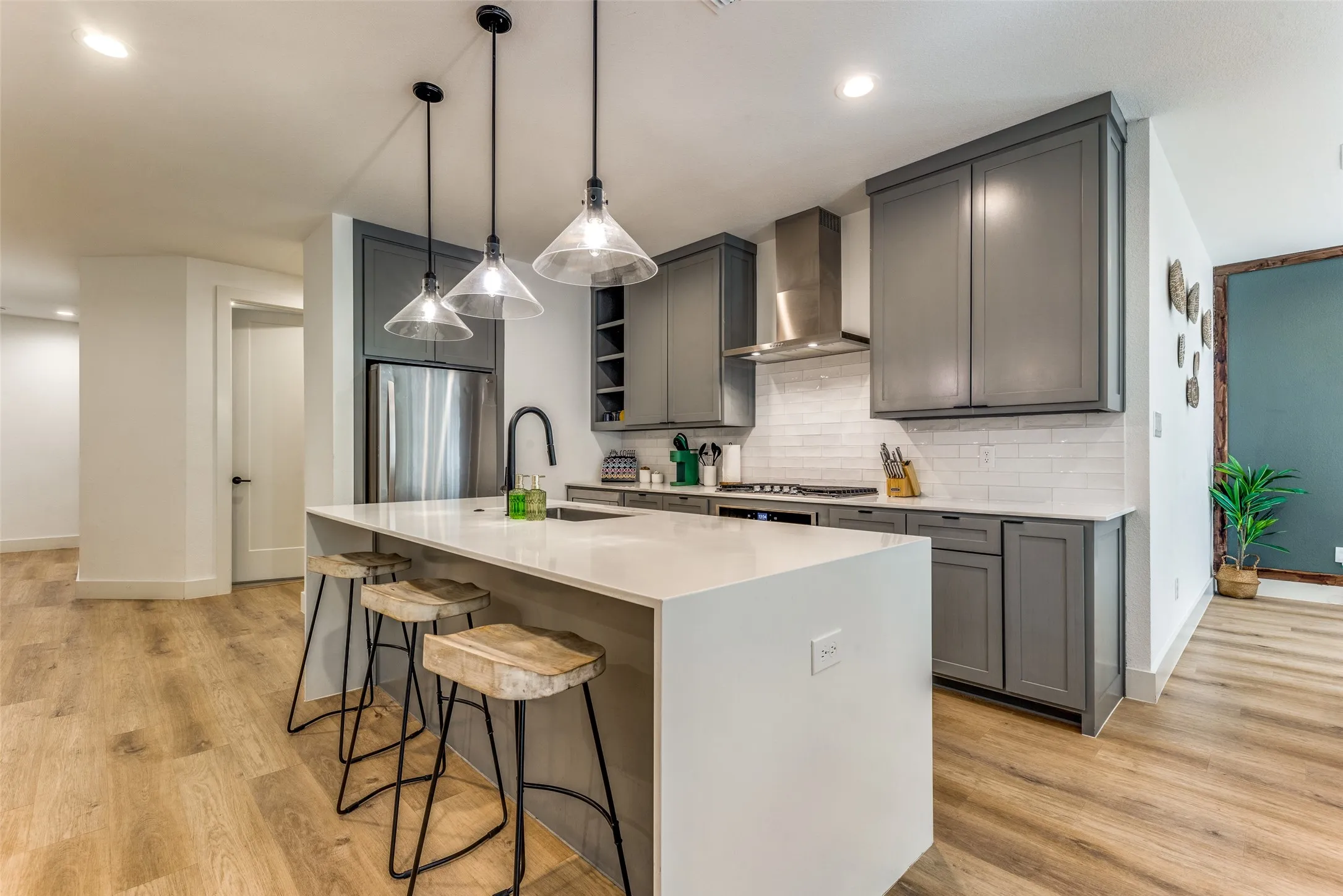 Modern kitchen featuring a large island with white countertop, gray cabinetry, stainless steel appliances, a subway tile backsplash, and wood-finish flooring