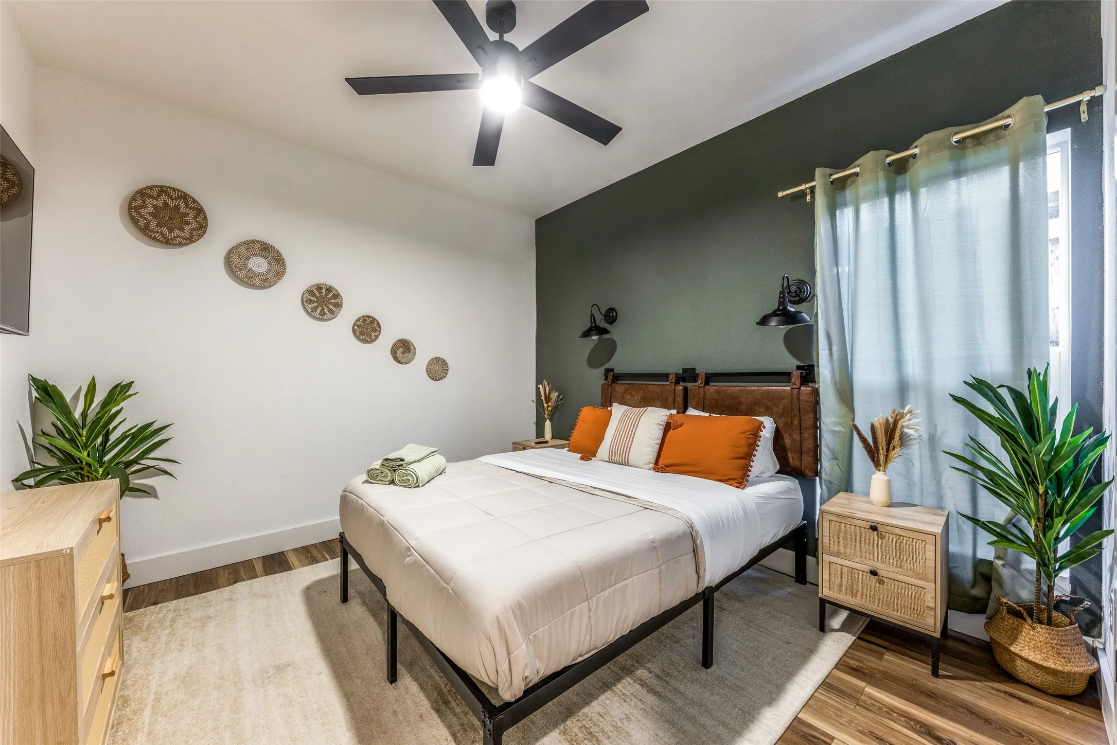 Bedroom featuring a dark accent wall, ceiling fan, wood-finish flooring, and a large window with drapes