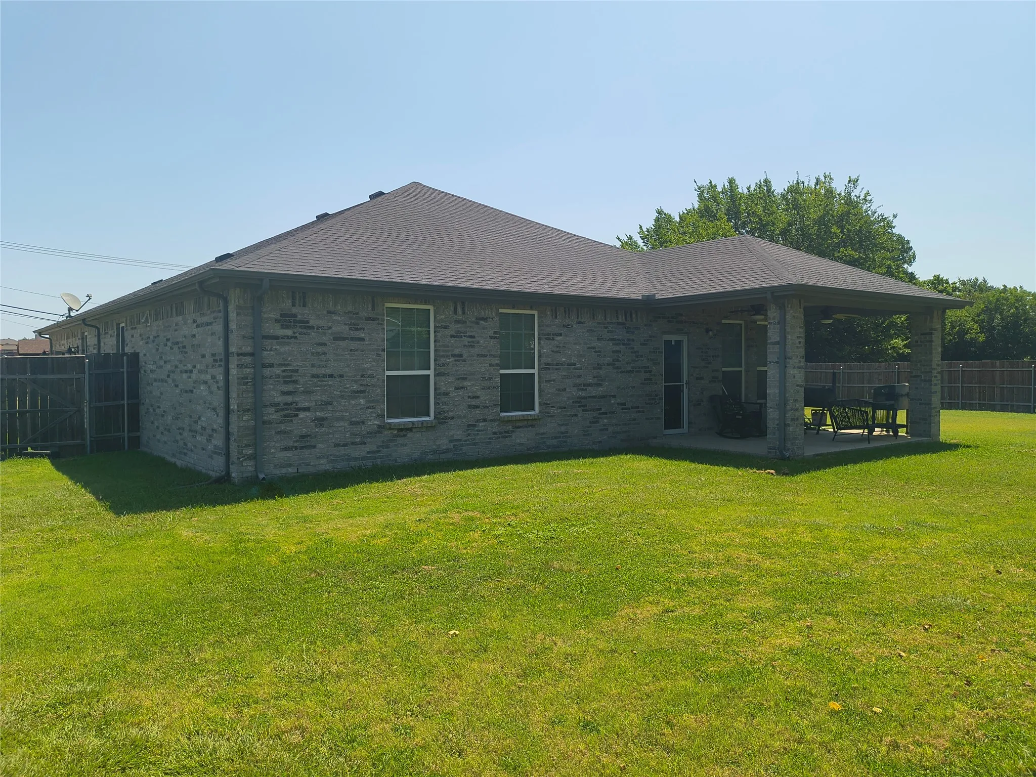 Expansive backyard featuring a covered patio with a concrete slab, durable brick exterior, and a dark shingle roof