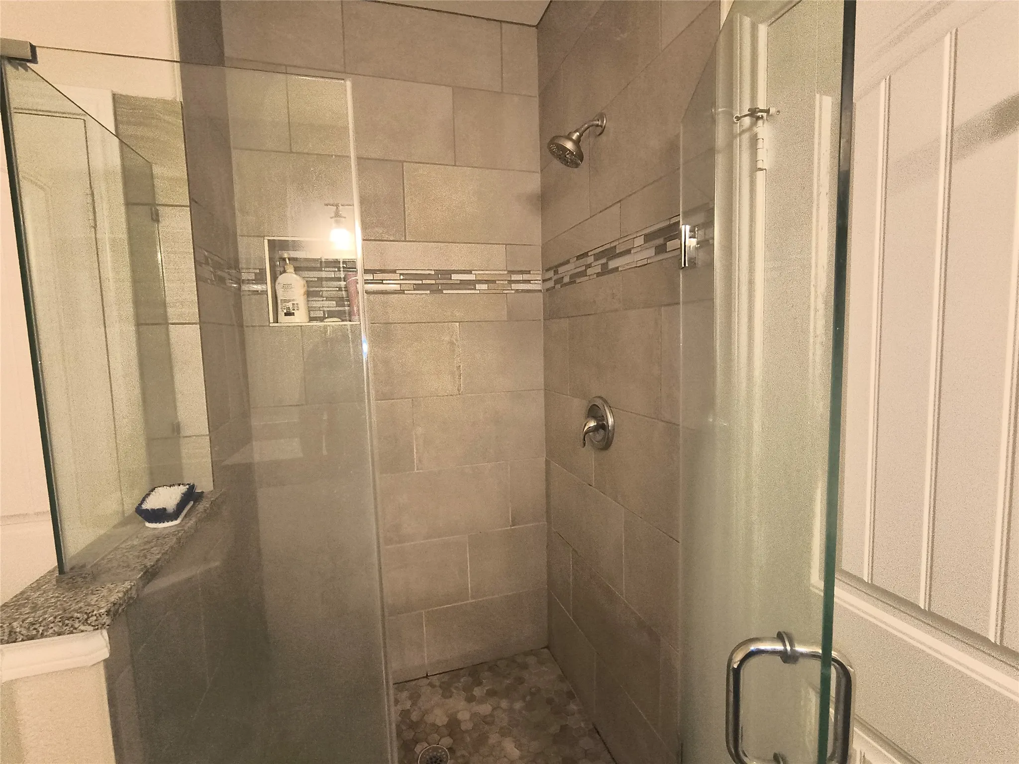 Shower enclosure with clear glass panels, subway-style wall tiling, mosaic accent band, built-in recessed shelf, and hexagonal floor tiling
