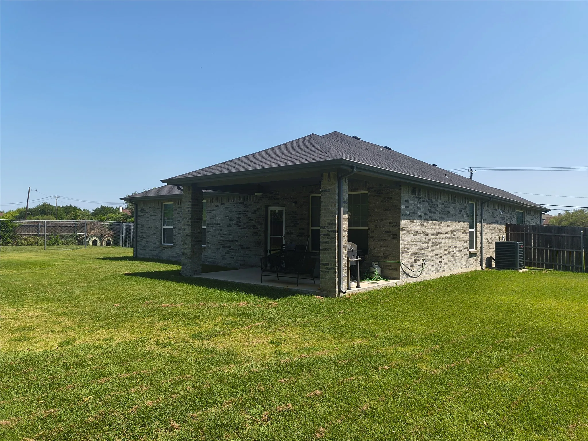 Spacious backyard featuring a covered patio, brick exterior, dark shingle roof, and a wood privacy fence