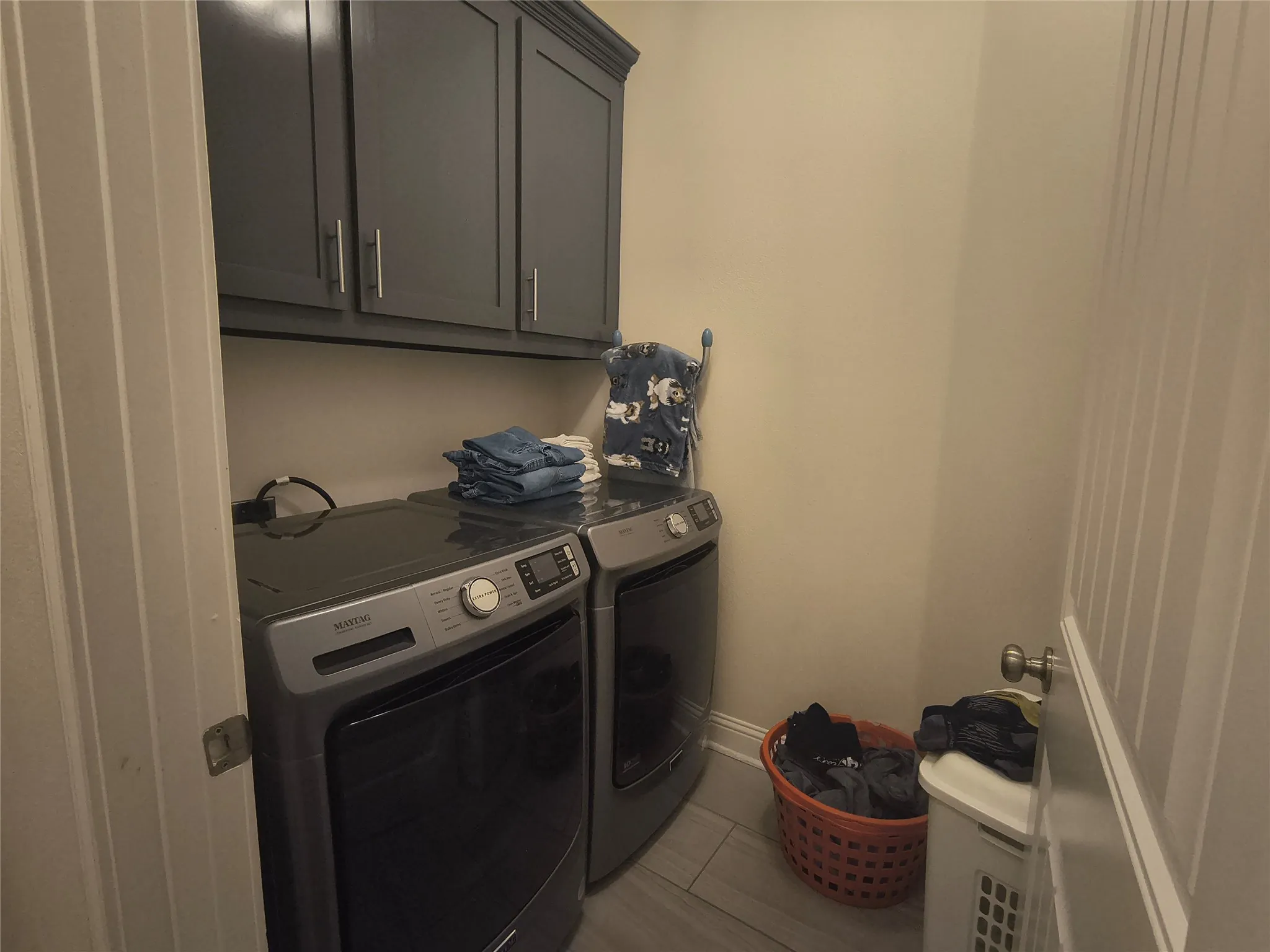 Dedicated laundry area featuring overhead cabinetry, tile flooring, and neutral wall tones