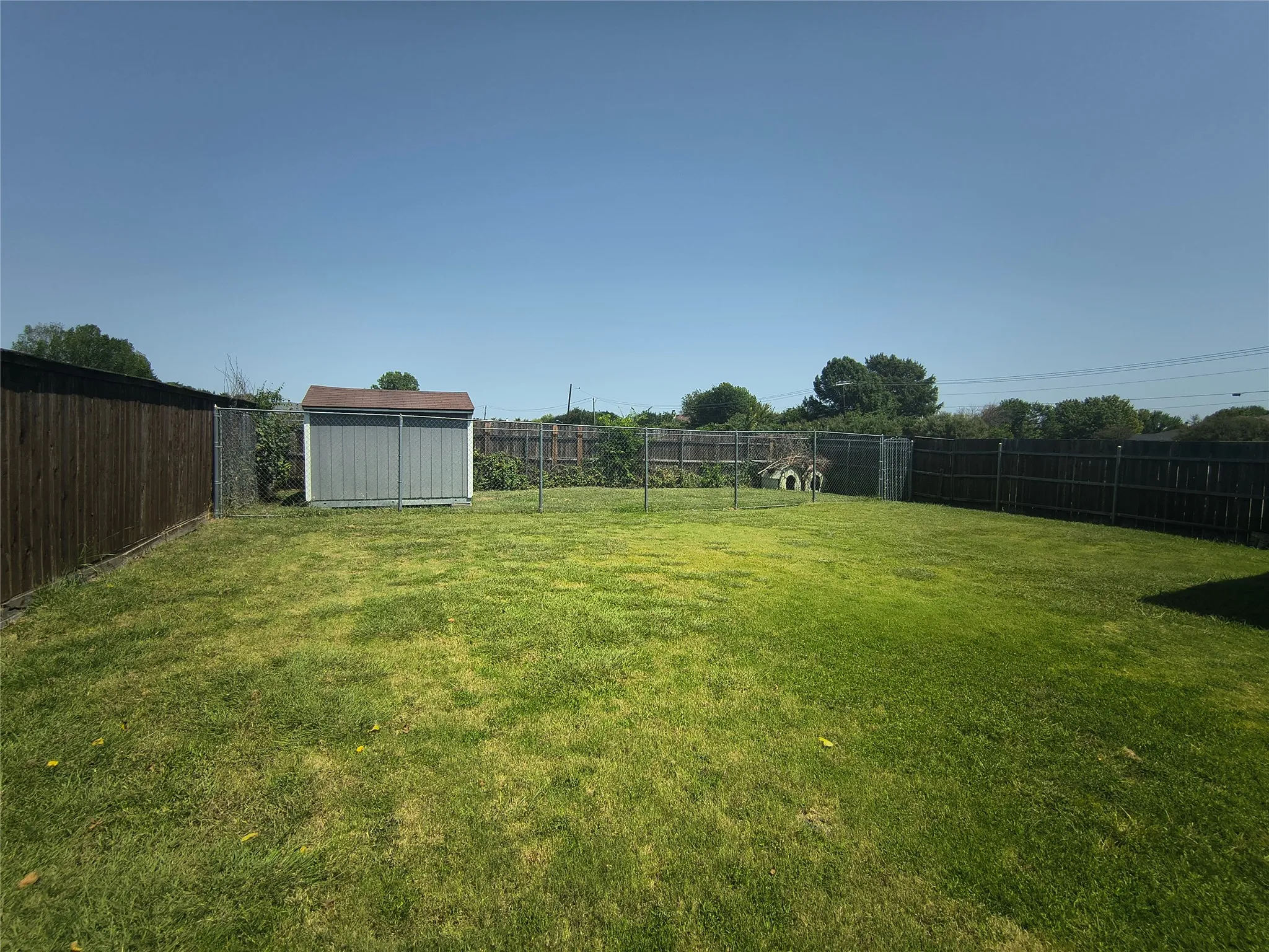 Expansive backyard featuring a lush lawn, a storage shed, and perimeter fencing