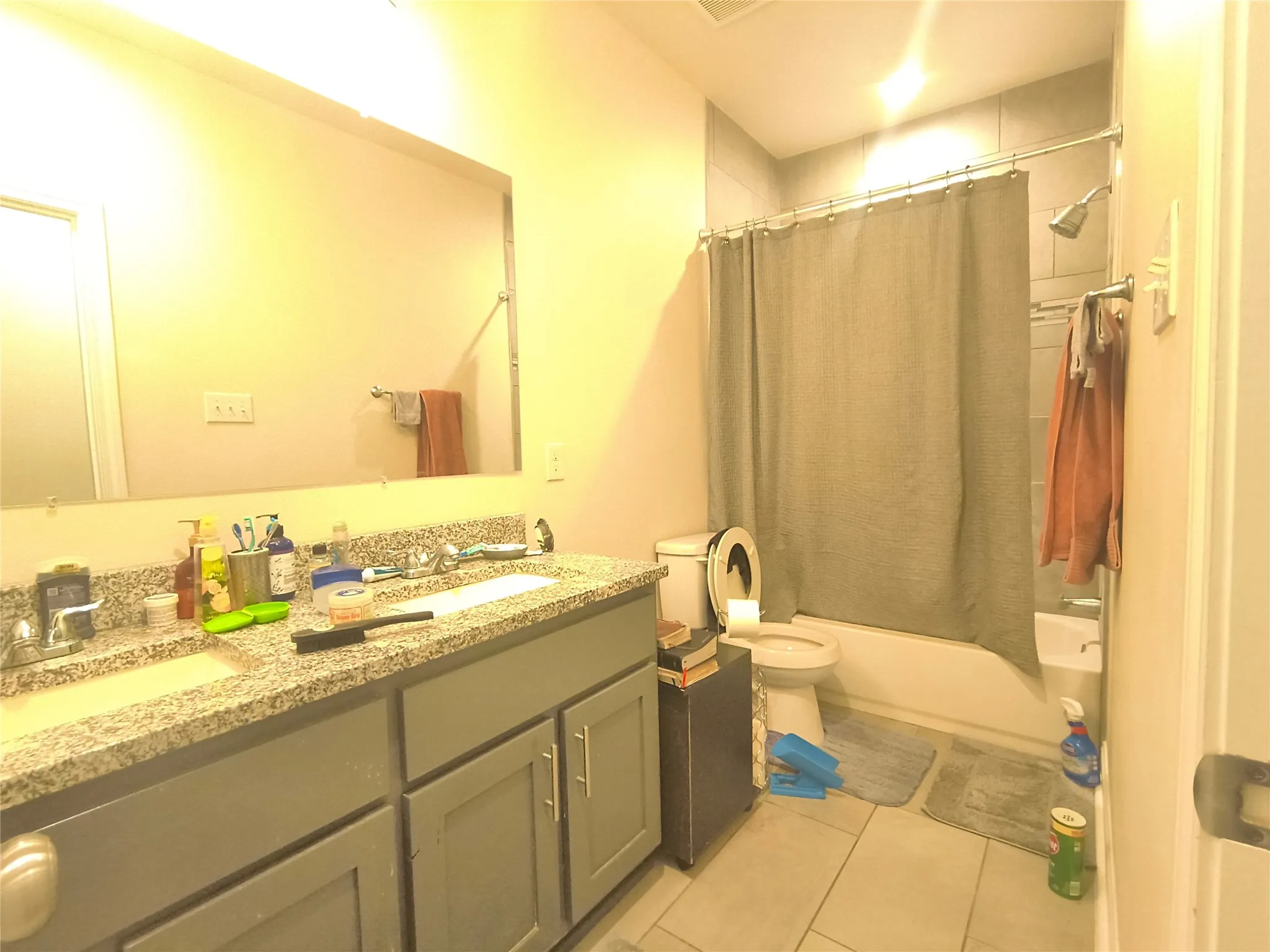 Bathroom featuring a dual-sink vanity with a granite-style countertop, gray cabinetry, a tub/shower combination with subway tile surround, and light-toned floor tile