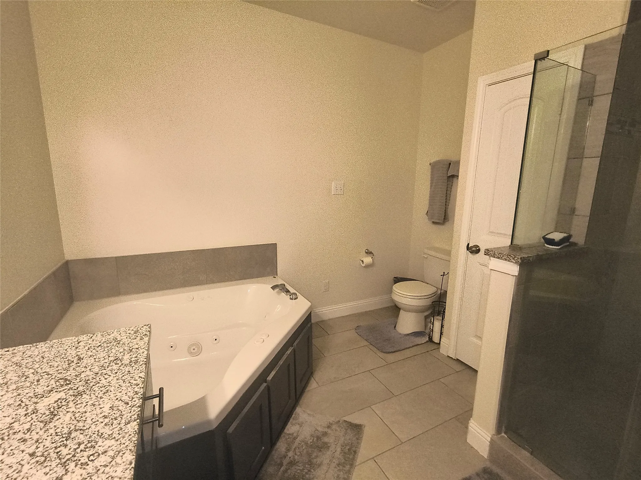 Spa-inspired bathroom featuring a corner jetted bathtub, a separate shower with glass enclosure, granite-finish countertops, and large format tile flooring