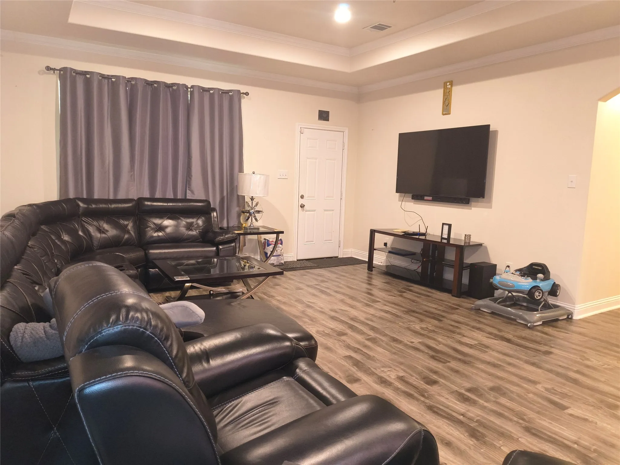 Spacious living area featuring wood-finish flooring, a tray ceiling, and crown molding