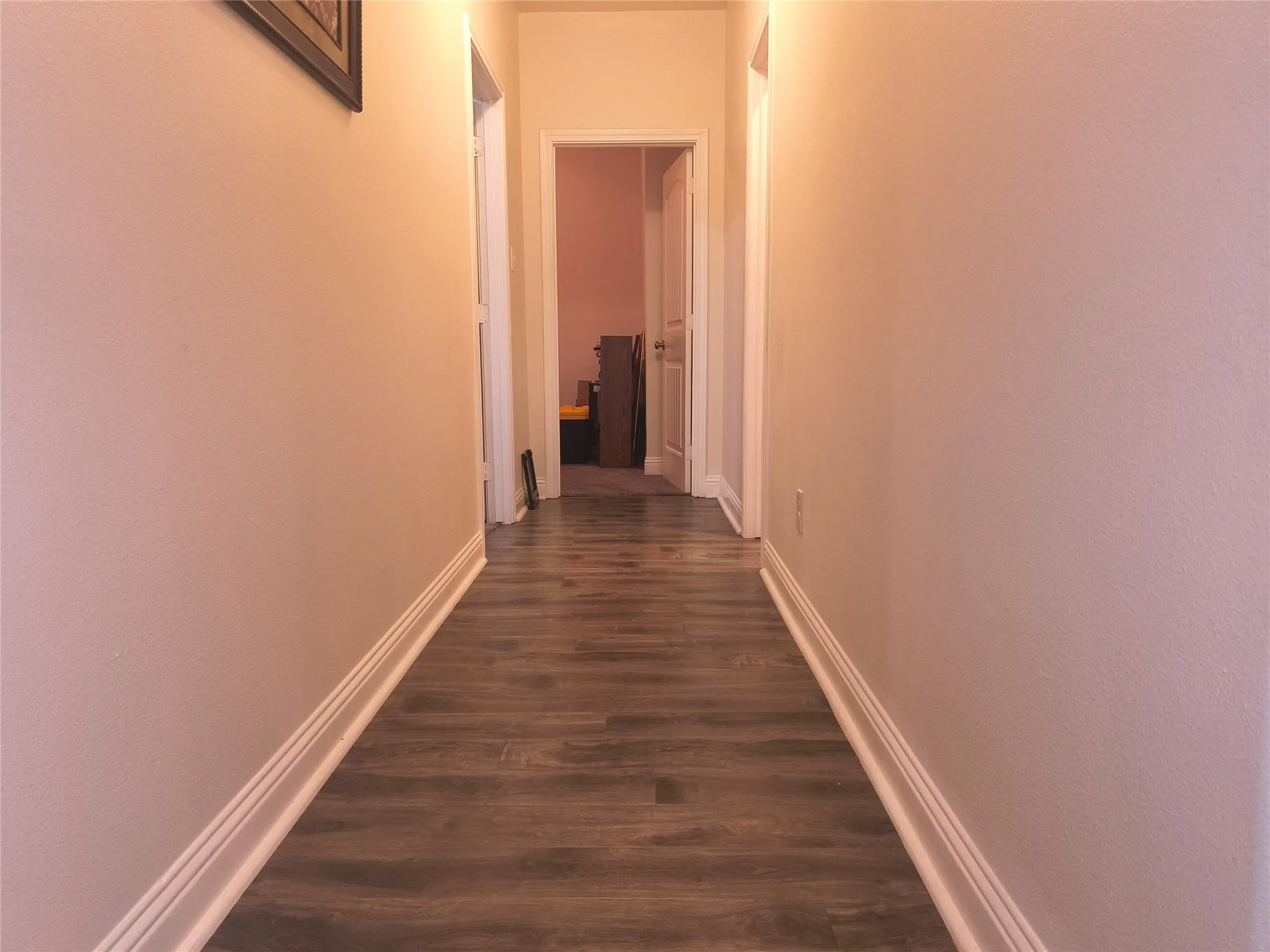 Hallway featuring wood-finish flooring and light-toned walls with white baseboards