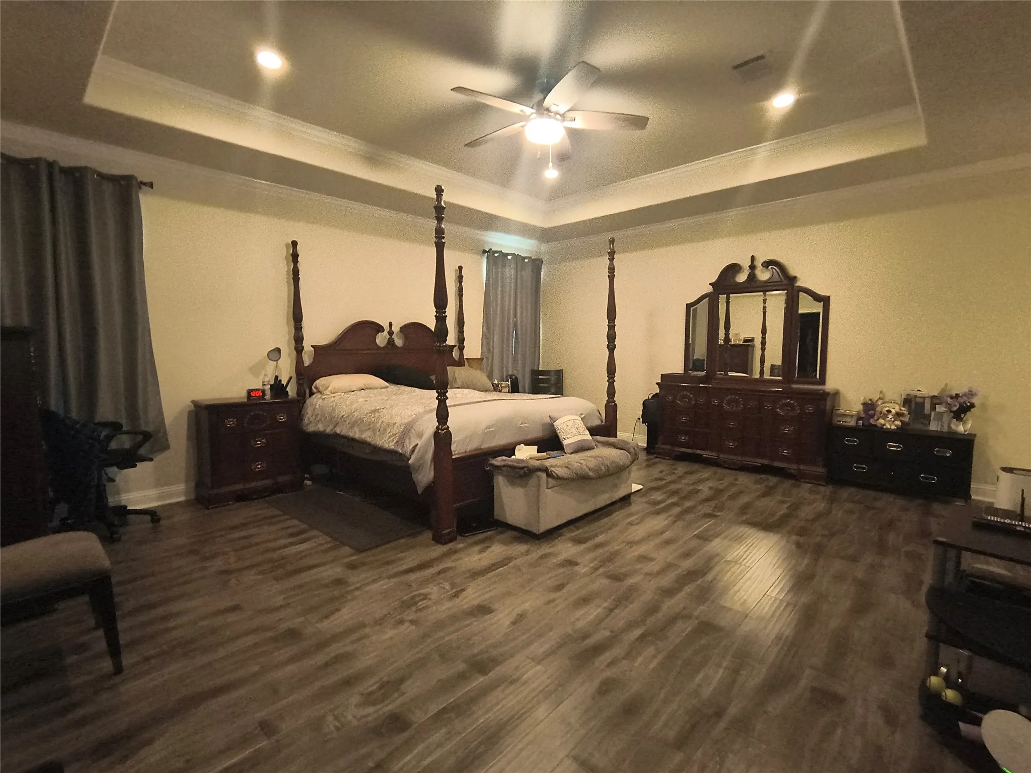 Spacious room featuring wood-finish flooring, a tray ceiling with recessed lighting, and a ceiling fan
