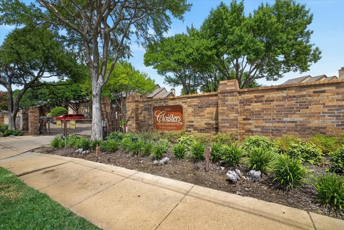 Brick perimeter wall with an integrated sign, mature trees, and established landscaping
