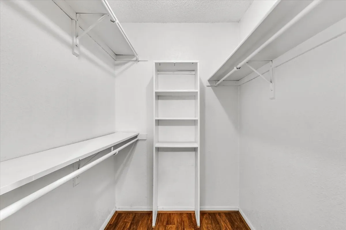 Walk-in closet featuring wood-finish flooring, white shelving, and hanging rods