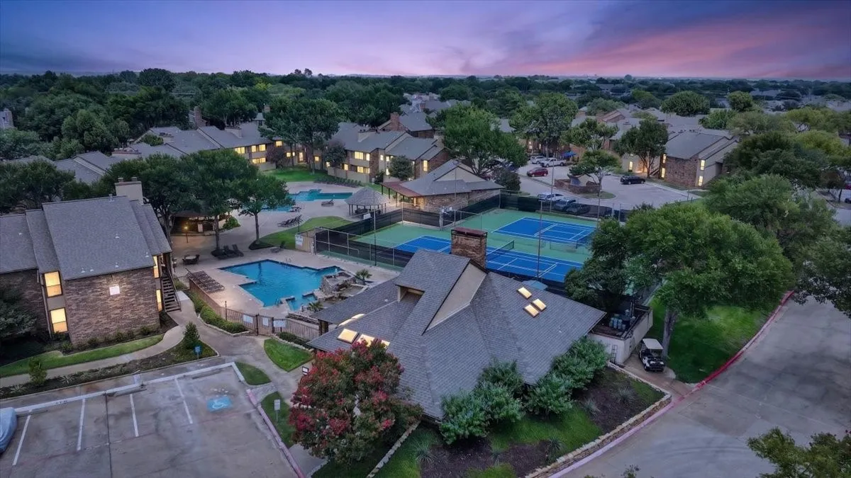 Aerial view showcasing expansive resort-style grounds featuring multiple illuminated swimming pools, tennis courts, mature landscaping throughout the property, and numerous residential structures nestled among lush tree canopy at twilight
