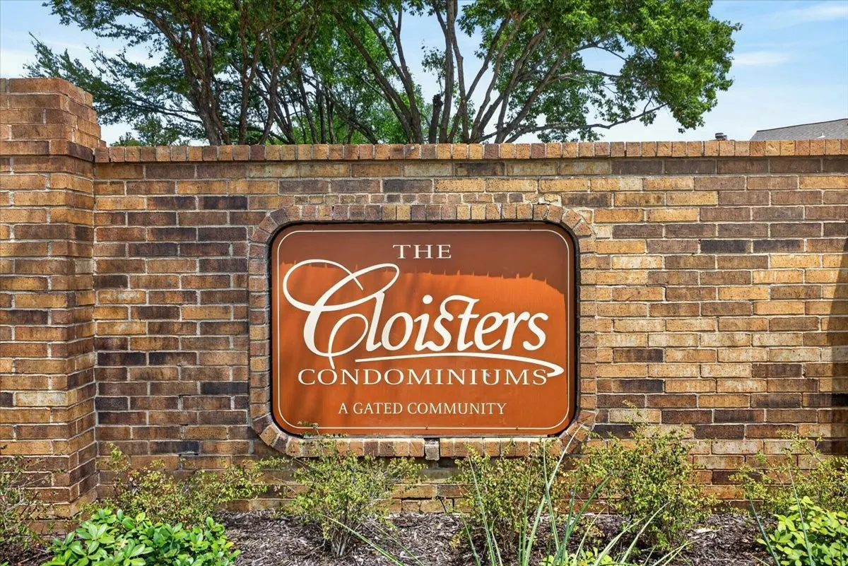 Brick wall entrance featuring a framed sign for "The Cloisters Condominiums," identifying it as a gated community