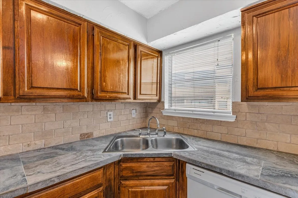 Kitchen featuring wood-finish cabinetry, a double-basin stainless steel sink, and a tiled backsplash.