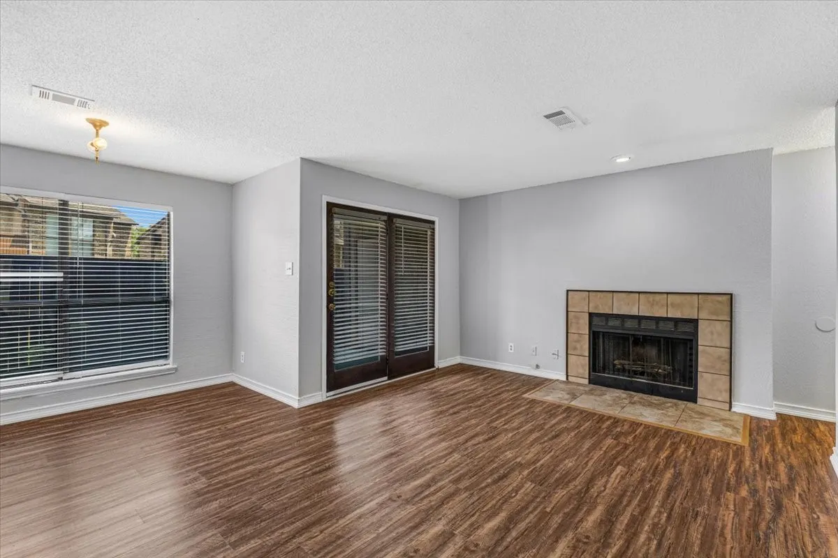 Wood-finish flooring, tiled fireplace with hearth, sliding glass doors, and a large window with blinds.