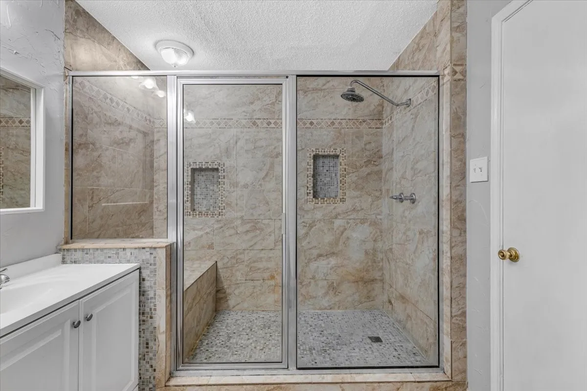 Glass-enclosed shower with a built-in bench, two tiled niches, and a rainfall showerhead.