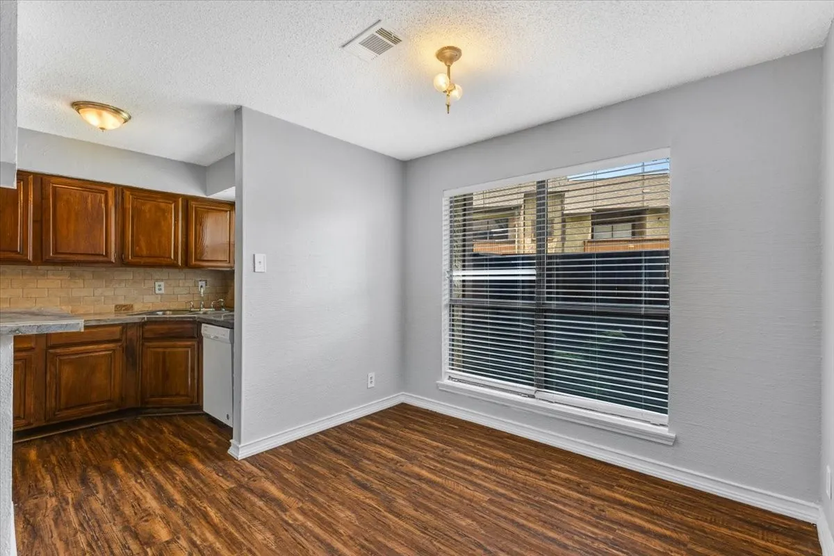 Kitchenette featuring wood-finish flooring, wood cabinetry, tile backsplash, and a built-in dishwasher.