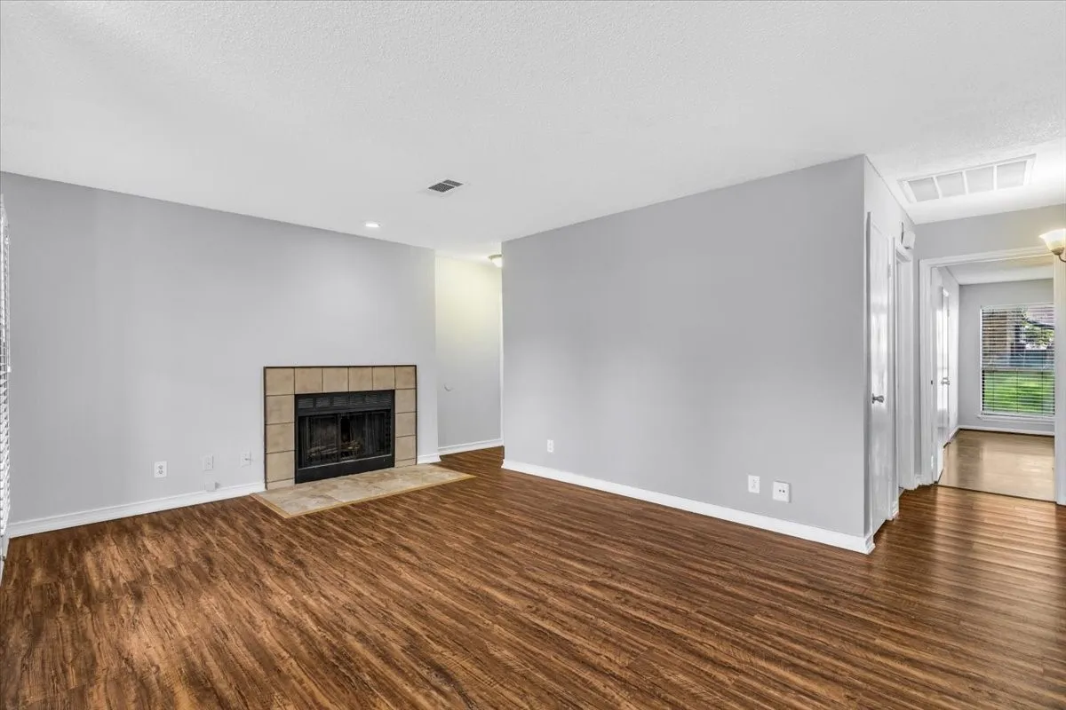 Fireplace with tile surround, wood-finish flooring, white walls, recessed ceiling lighting, and overhead lighting fixture.