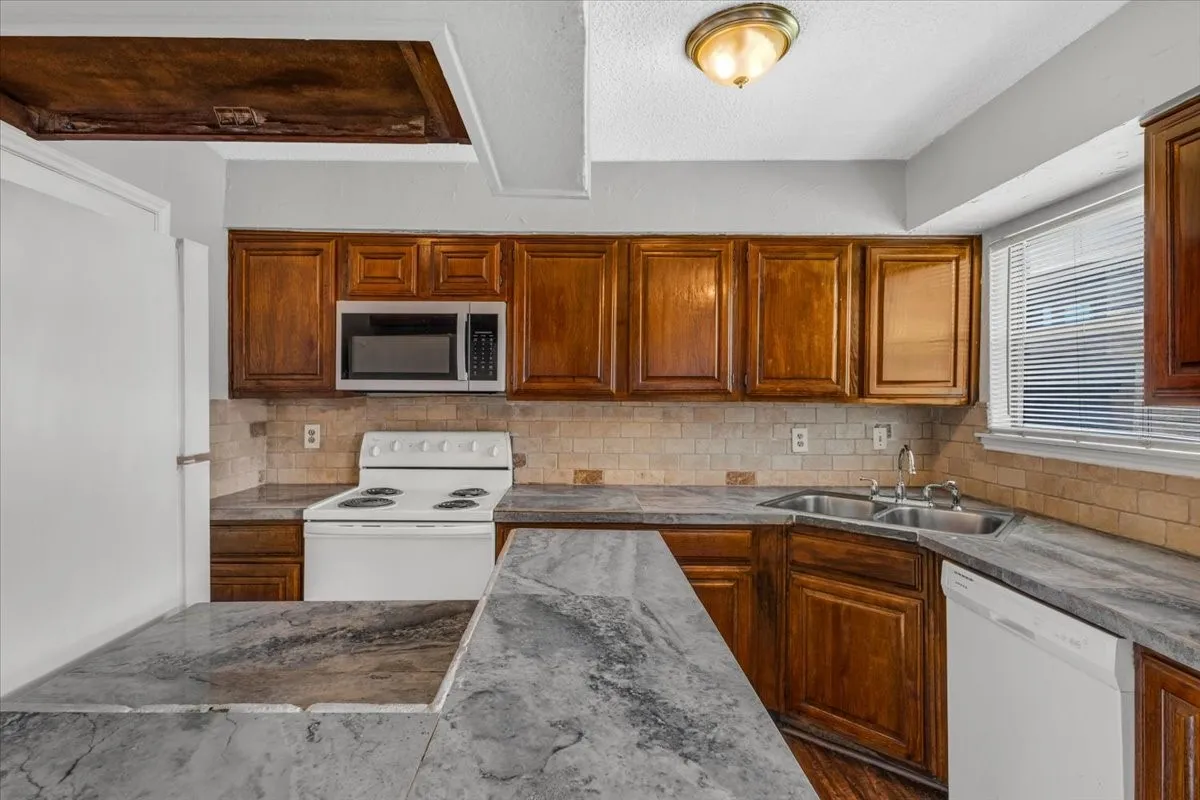 Wood-finish cabinetry paired with a tile backsplash, stainless steel double basin sink, and a built-in microwave.