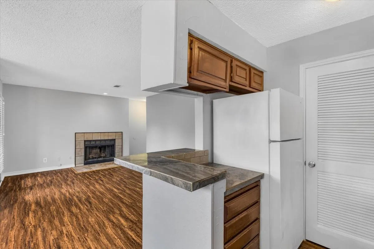 Open-concept kitchen and living area featuring wood-finish flooring, white cabinetry with stainless steel appliances, a center island with wood-grain countertop, and a range hood with chimney-style ventilation.