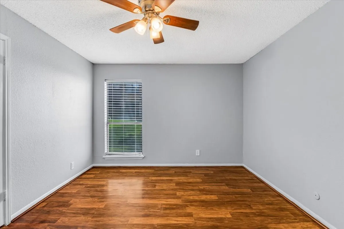 Wood-finish flooring, single window with blinds, ceiling fan with light fixture, and light gray wall paint