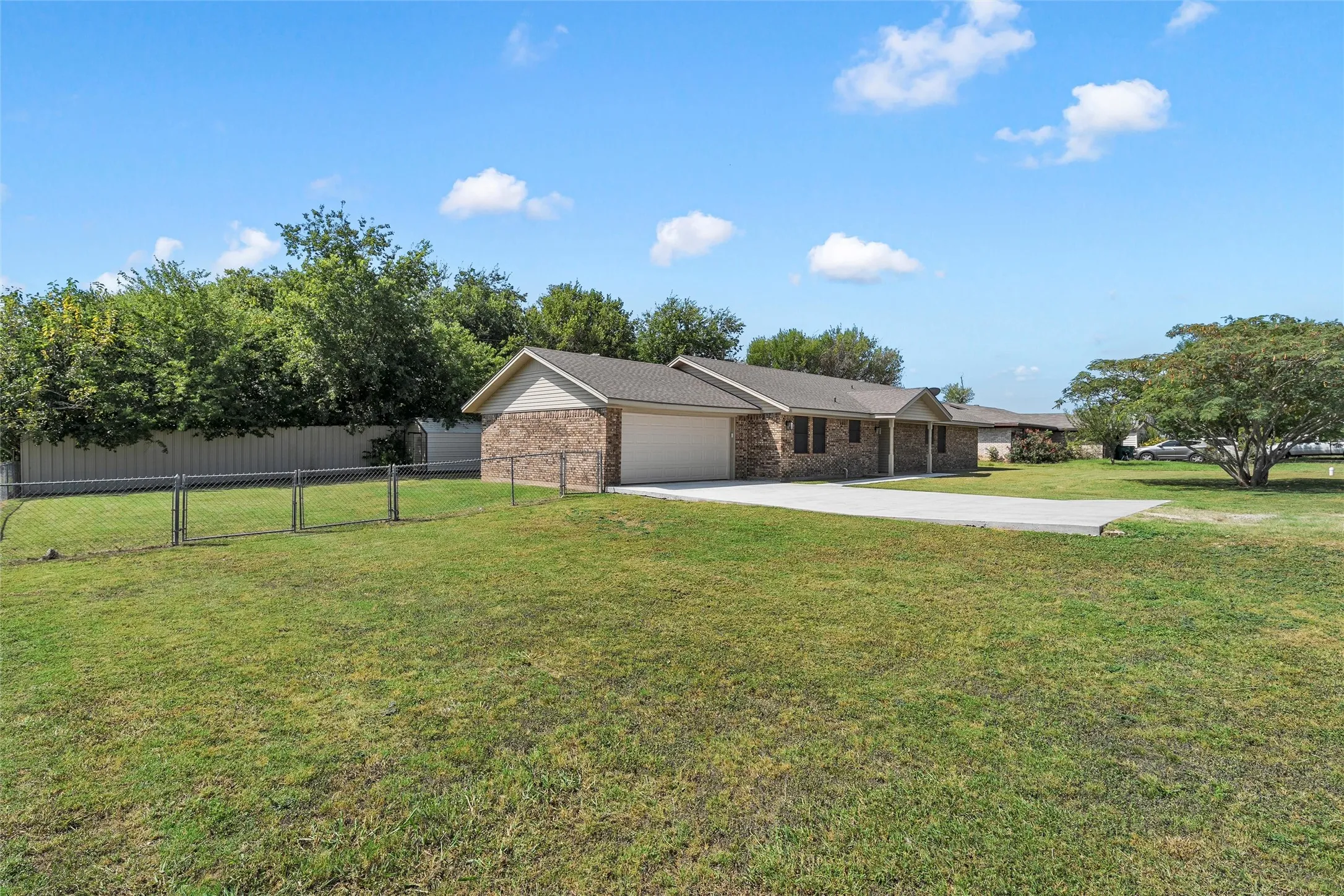 Brick facade home featuring an attached garage, concrete driveway, and expansive lawn