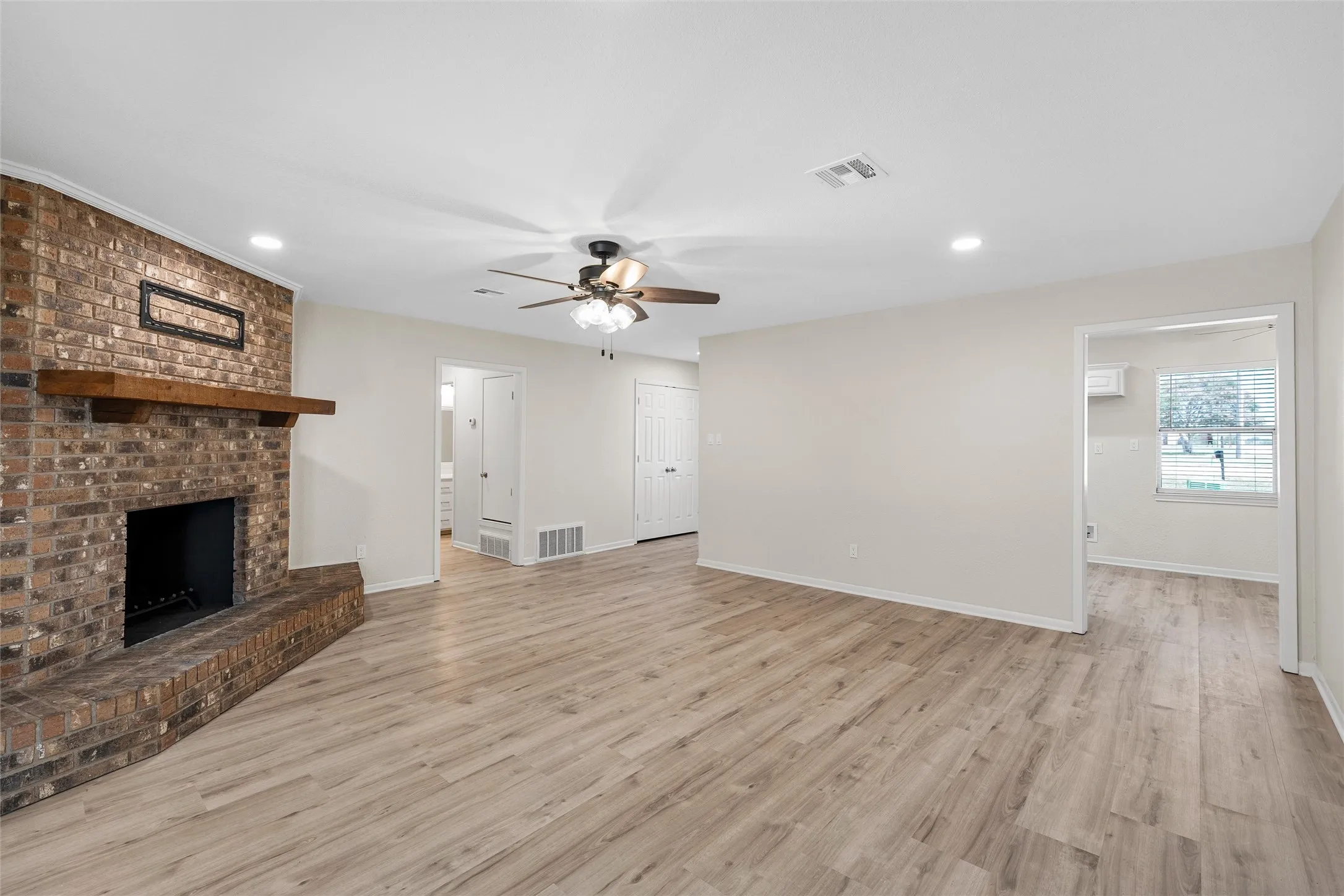Spacious living area featuring wood-finish flooring, a brick fireplace with a wood mantle, and recessed lighting