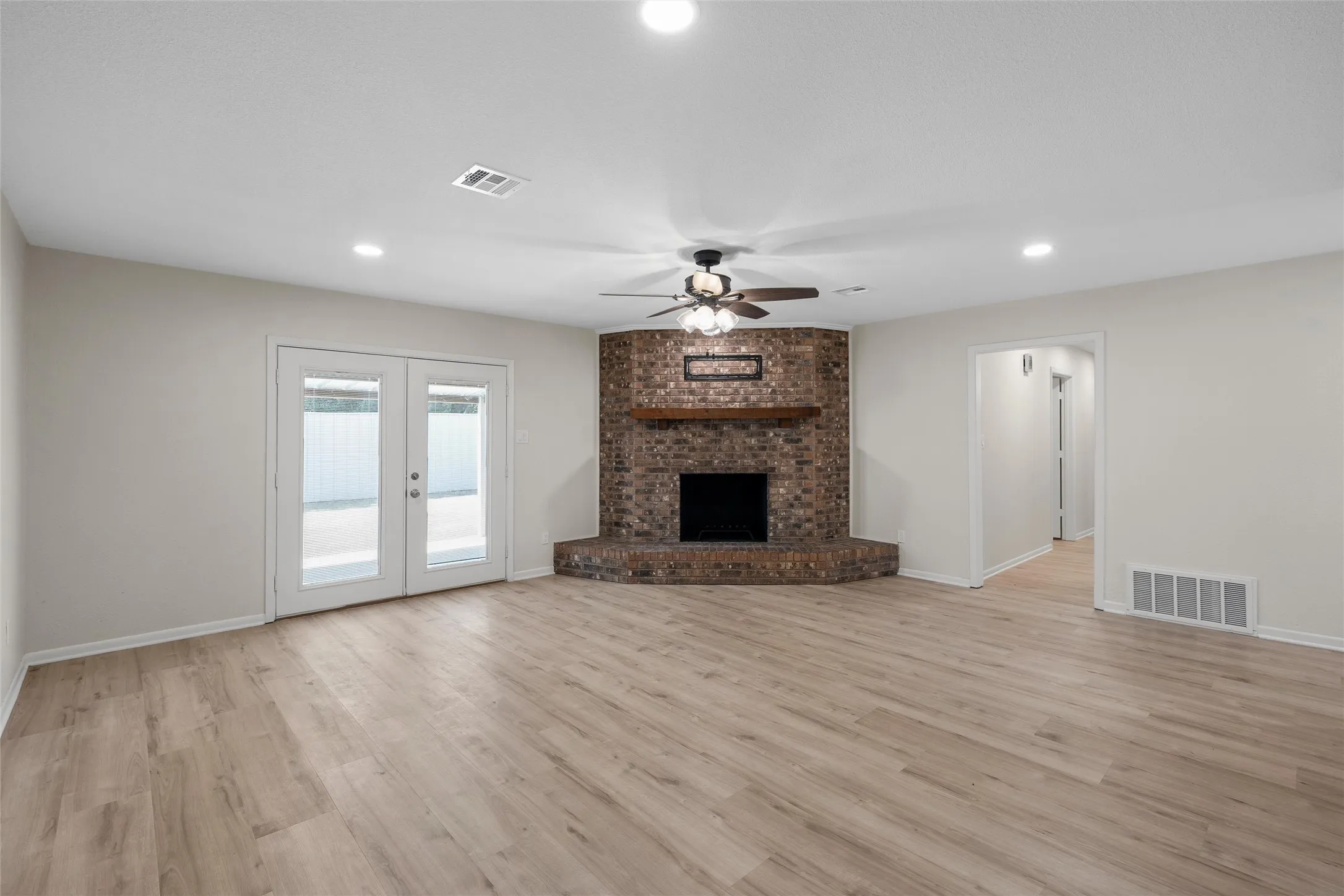 Spacious room featuring wood-finish flooring, a brick fireplace with a wood mantle, and bright recessed lighting