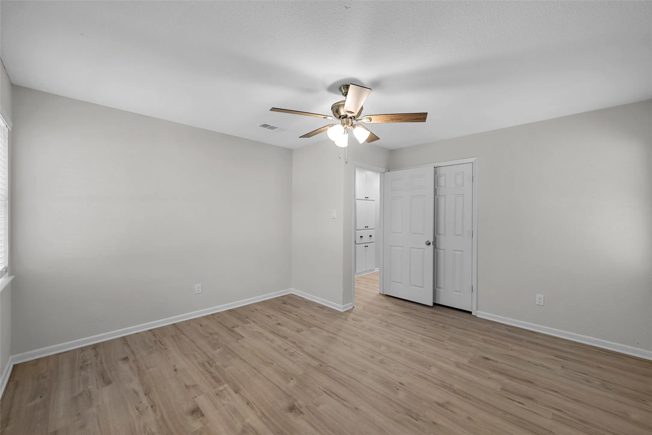 Spacious room featuring wood-finish flooring, light gray wall paint, and a ceiling fan with light fixture