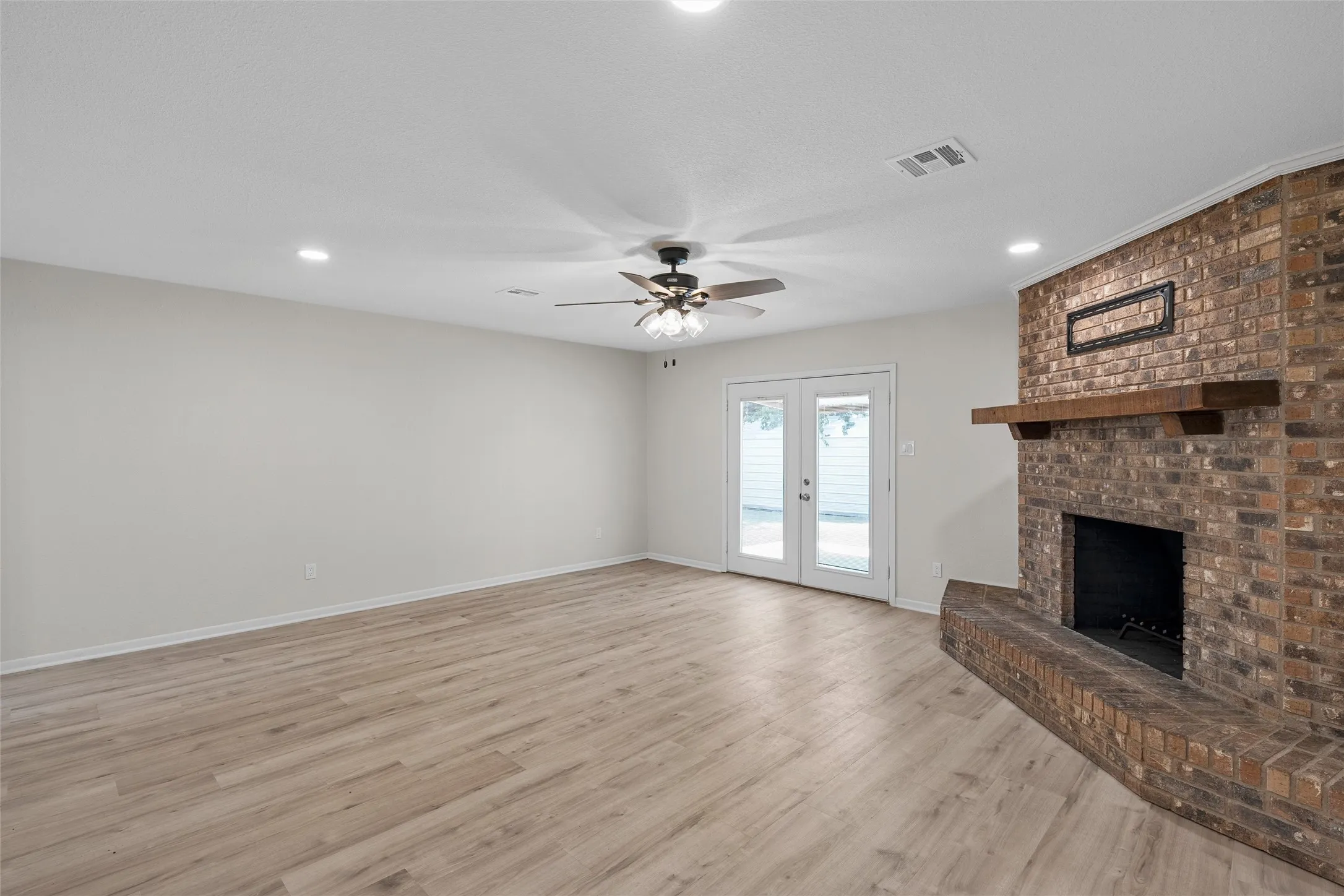 Spacious room featuring wood-finish flooring, a brick fireplace with wood mantel, recessed lighting, and a ceiling fan