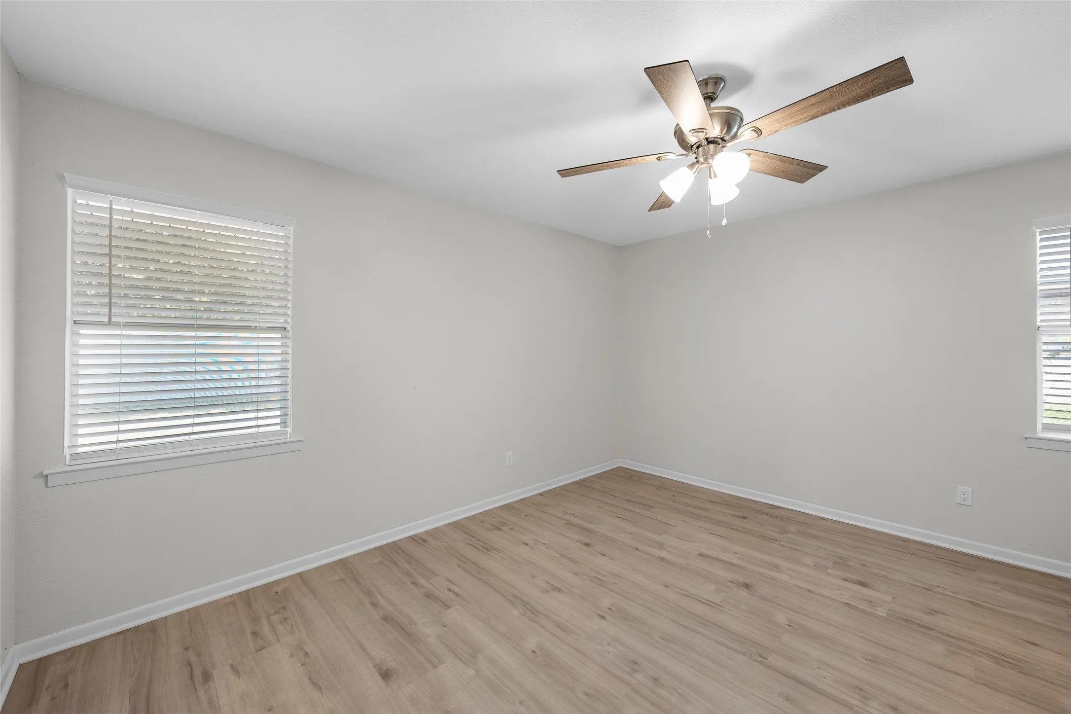 Spacious interior room featuring light wood-finish flooring, white walls, and a ceiling fan with integrated lighting